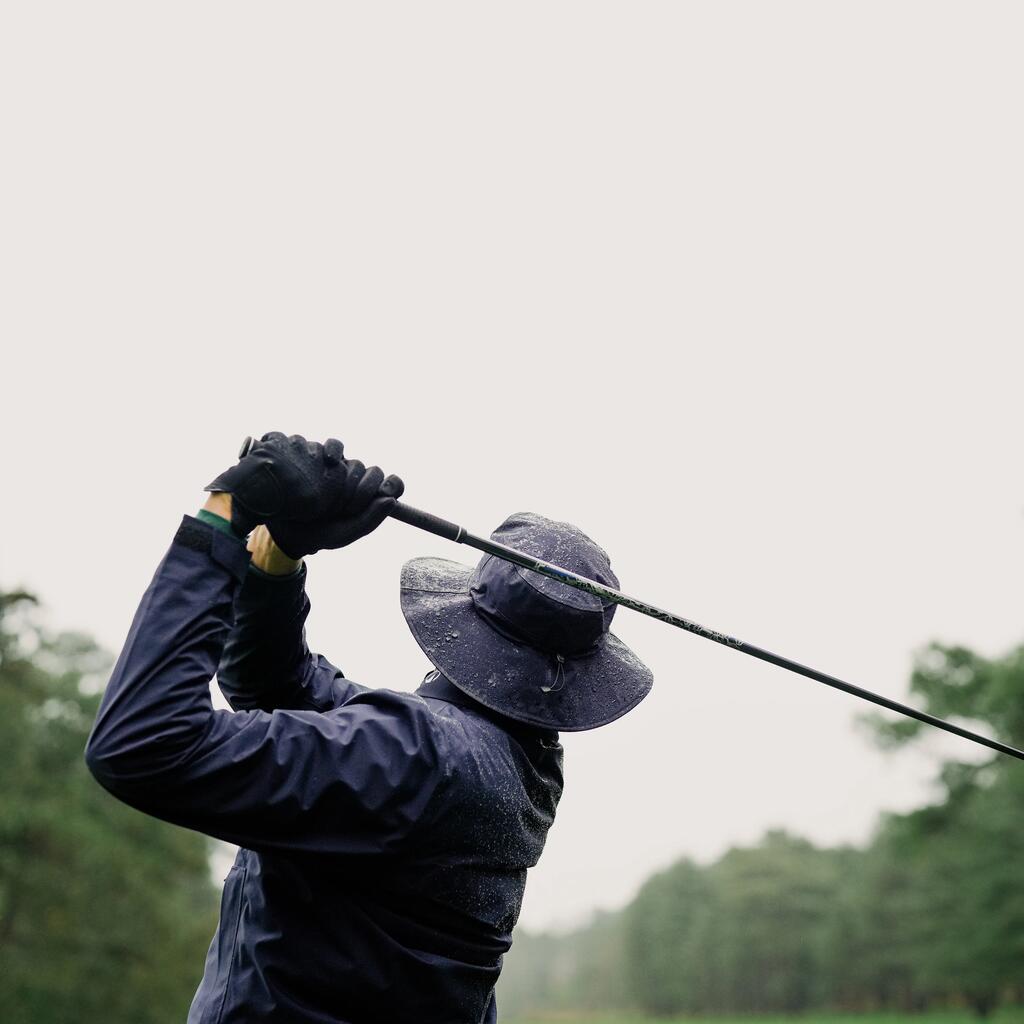Rückansicht eines Golfspielers in wetterfester Kleidung mit Hut, der im Regen zum Schwung ausholt.