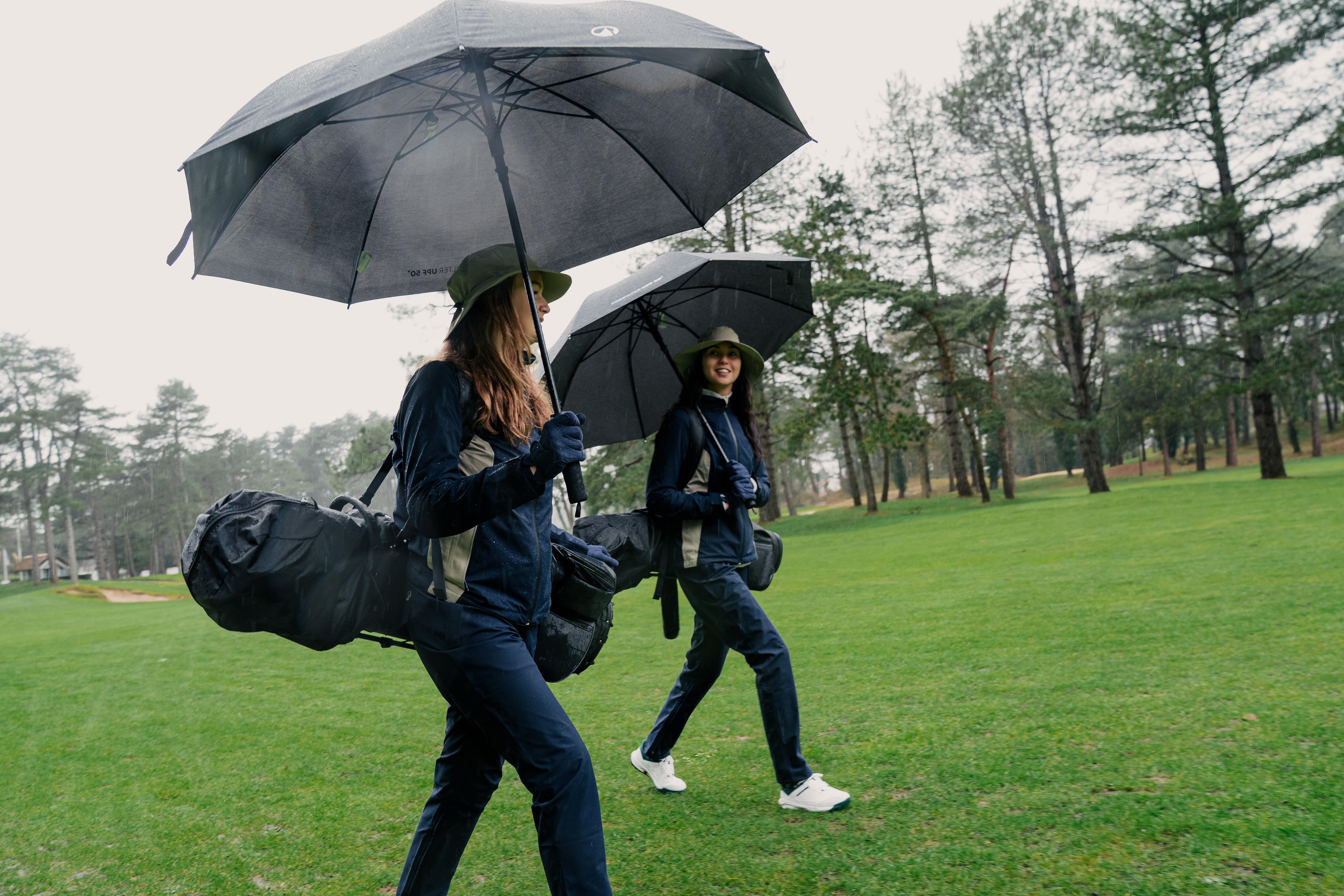 Two women walking with golf umbrellas and golf bags on course