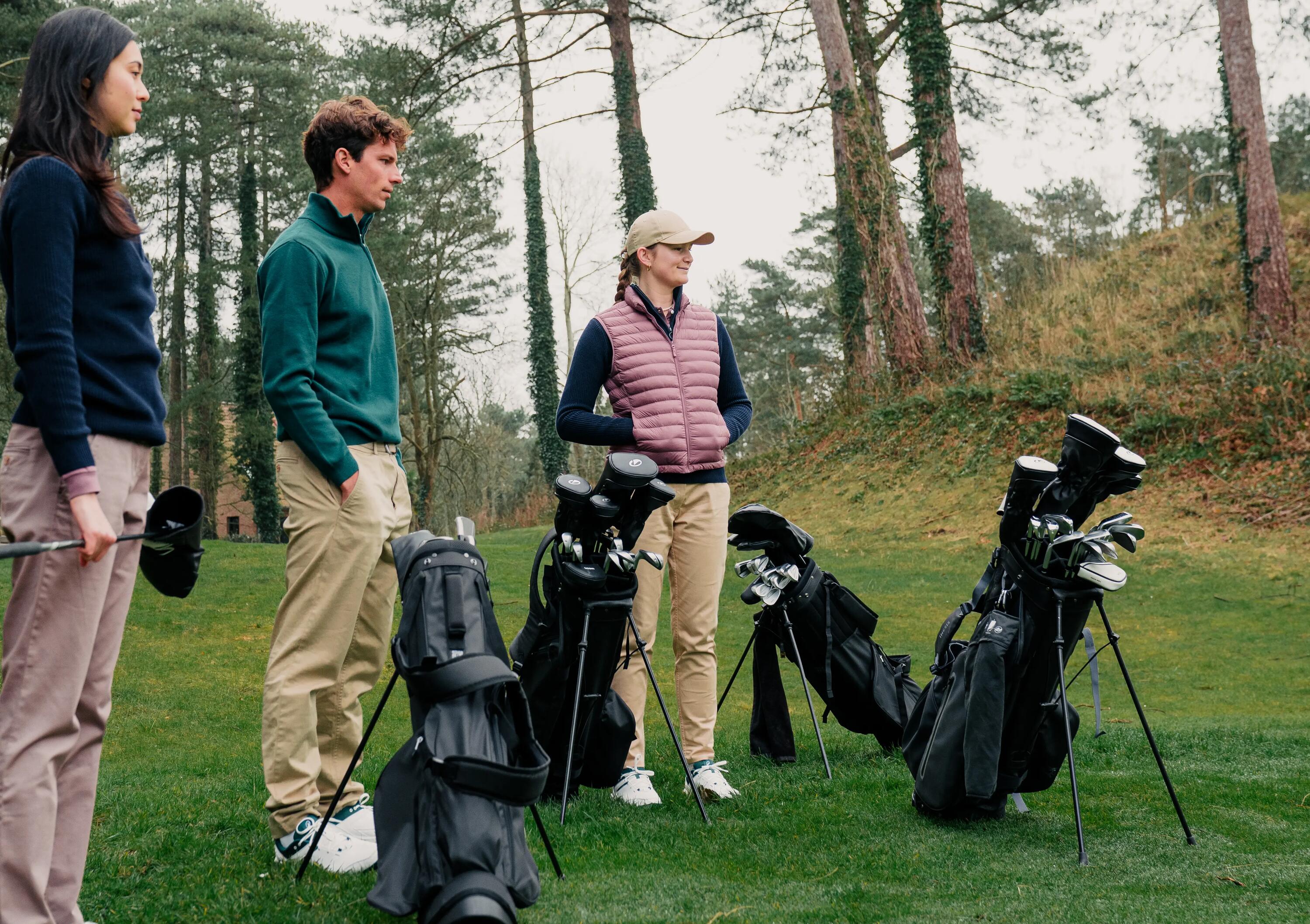 Drei Personen stehen mit ihren Golftaschen auf einem grünen Golfplatz vor Bäumen.