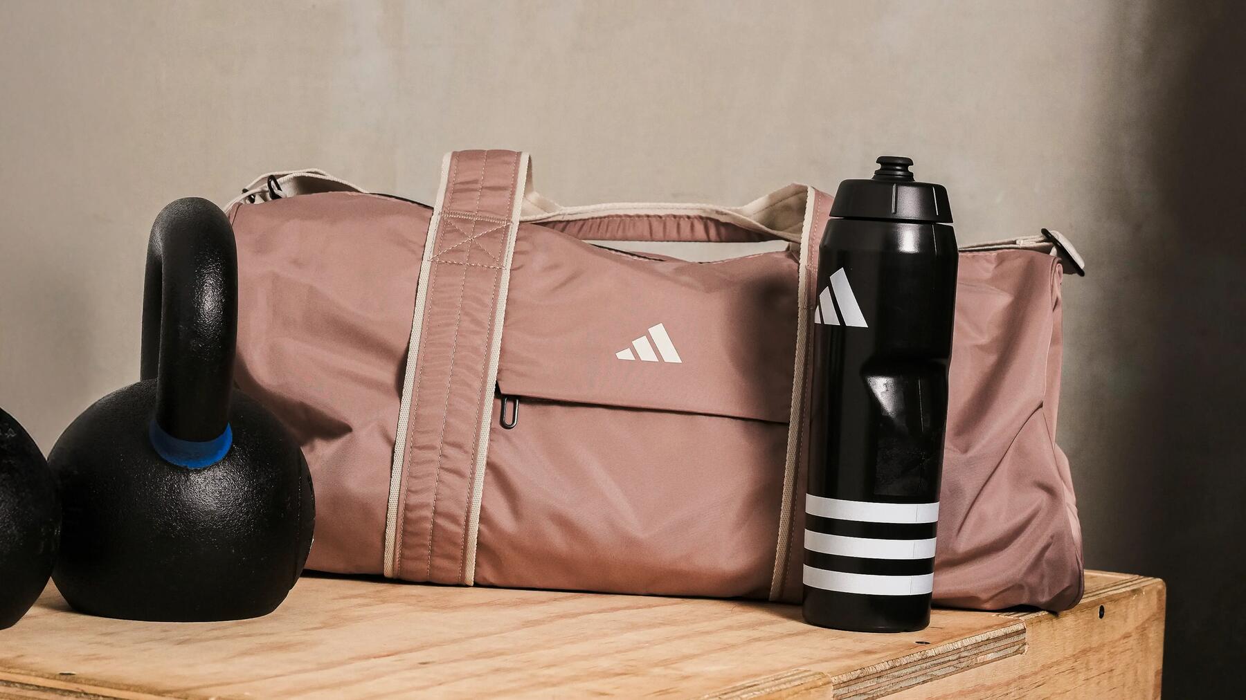 Eine Sporttasche als Teil der Fitness-Bekleidung für Damen steht zwischen Gewicht und Flasche