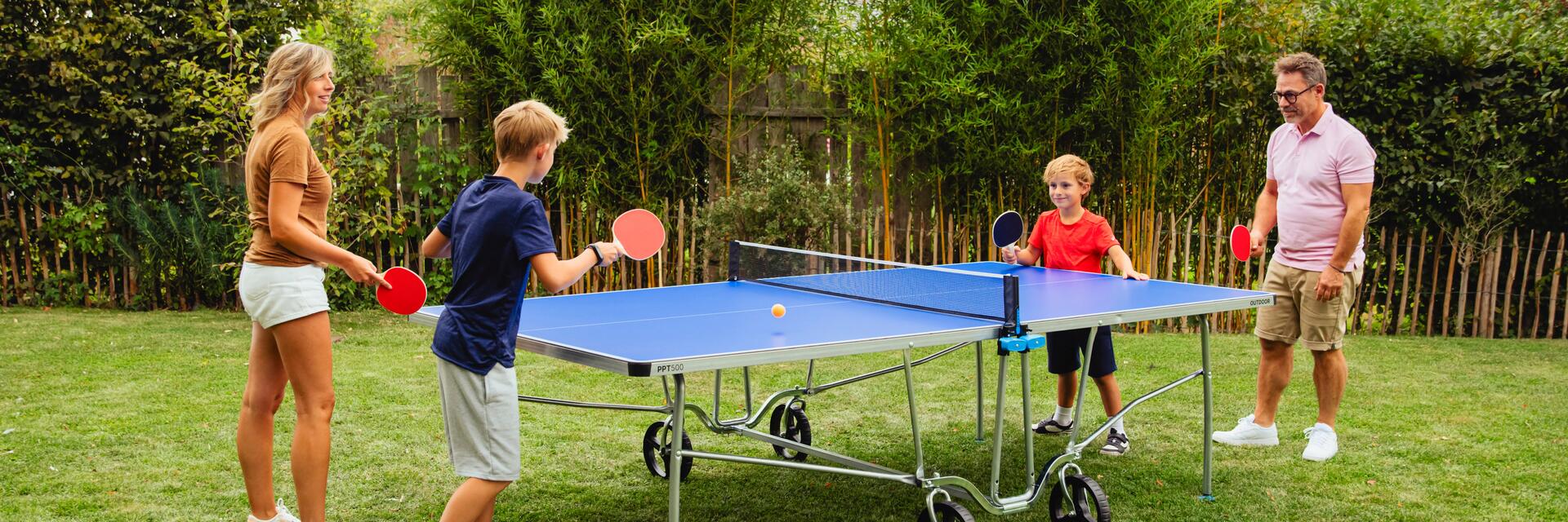 Eine Familie spielt in Garten an einer Tischtennisplatte Tischtennis.