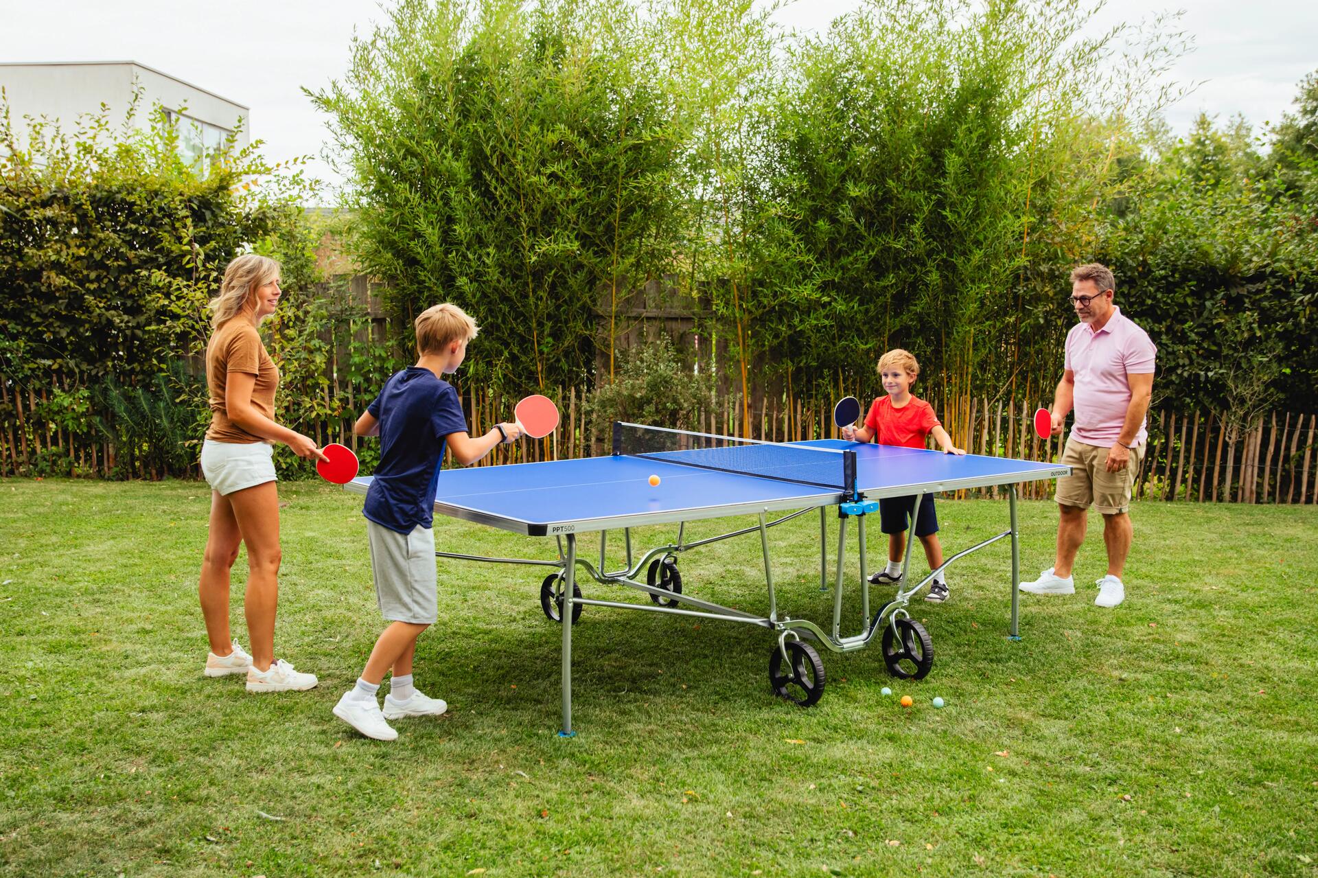 Eine Familie spielt in Garten an einer Tischtennisplatte Tischtennis.