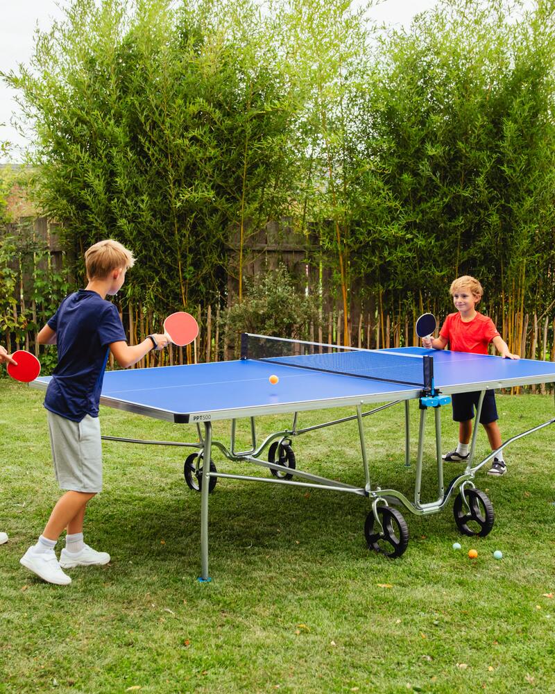 Eine Familie spielt in Garten an einer Tischtennisplatte Tischtennis.