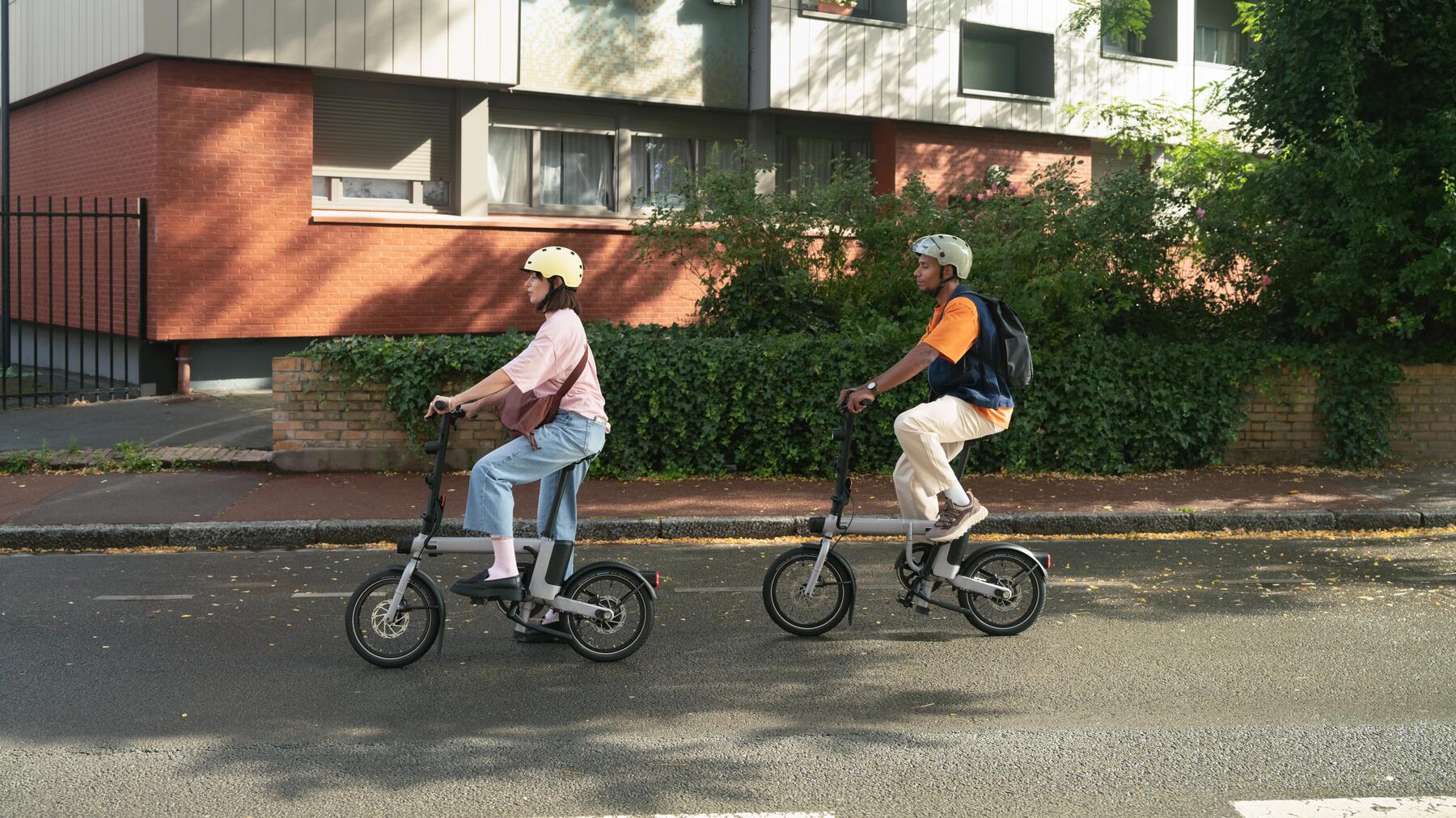 Zwei Freunde fahren vor einem Haus mit ihren Klapprädern