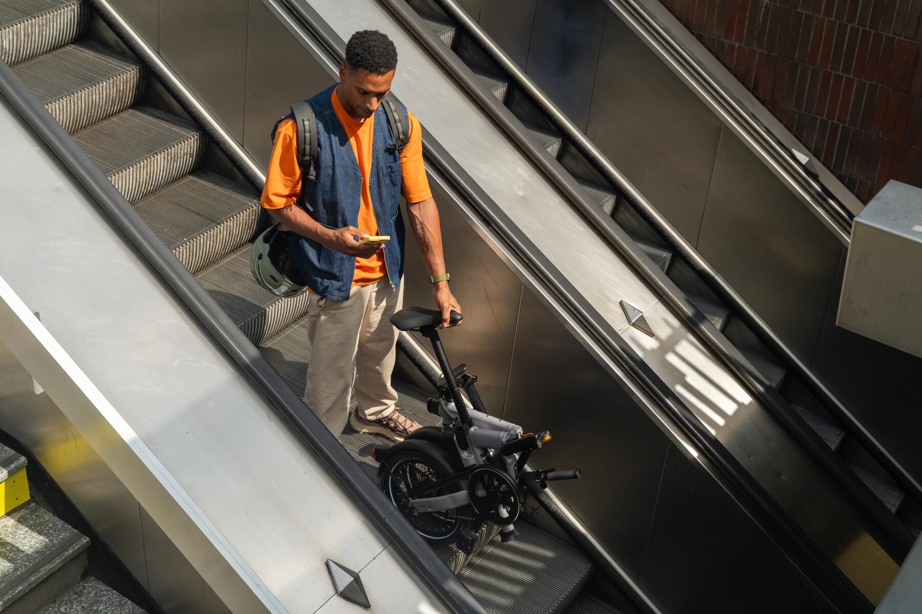 Ein Mann hat sein Klapprad auf der Rolltreppe dabei