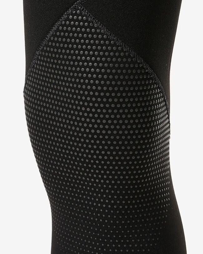 Zoom sur les renforts en picots de silicone au niveau du genou plié de la combinaison de plongée noire.