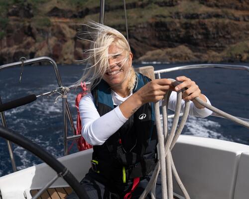 Seglerin mit Latzhose und Rettungsweste auf einem Boot, die ein Seil hält