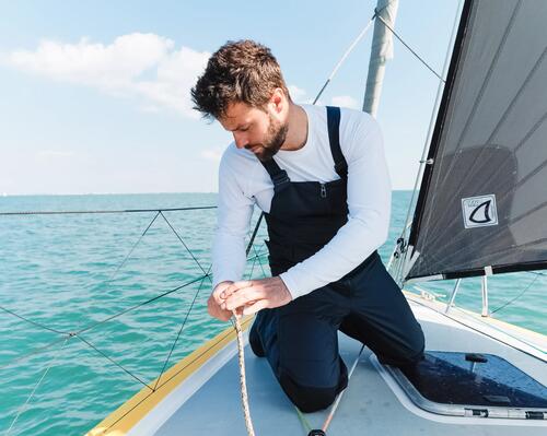 marin accroupi usr le bateau avec un bout à la main, il est en salopette de quart