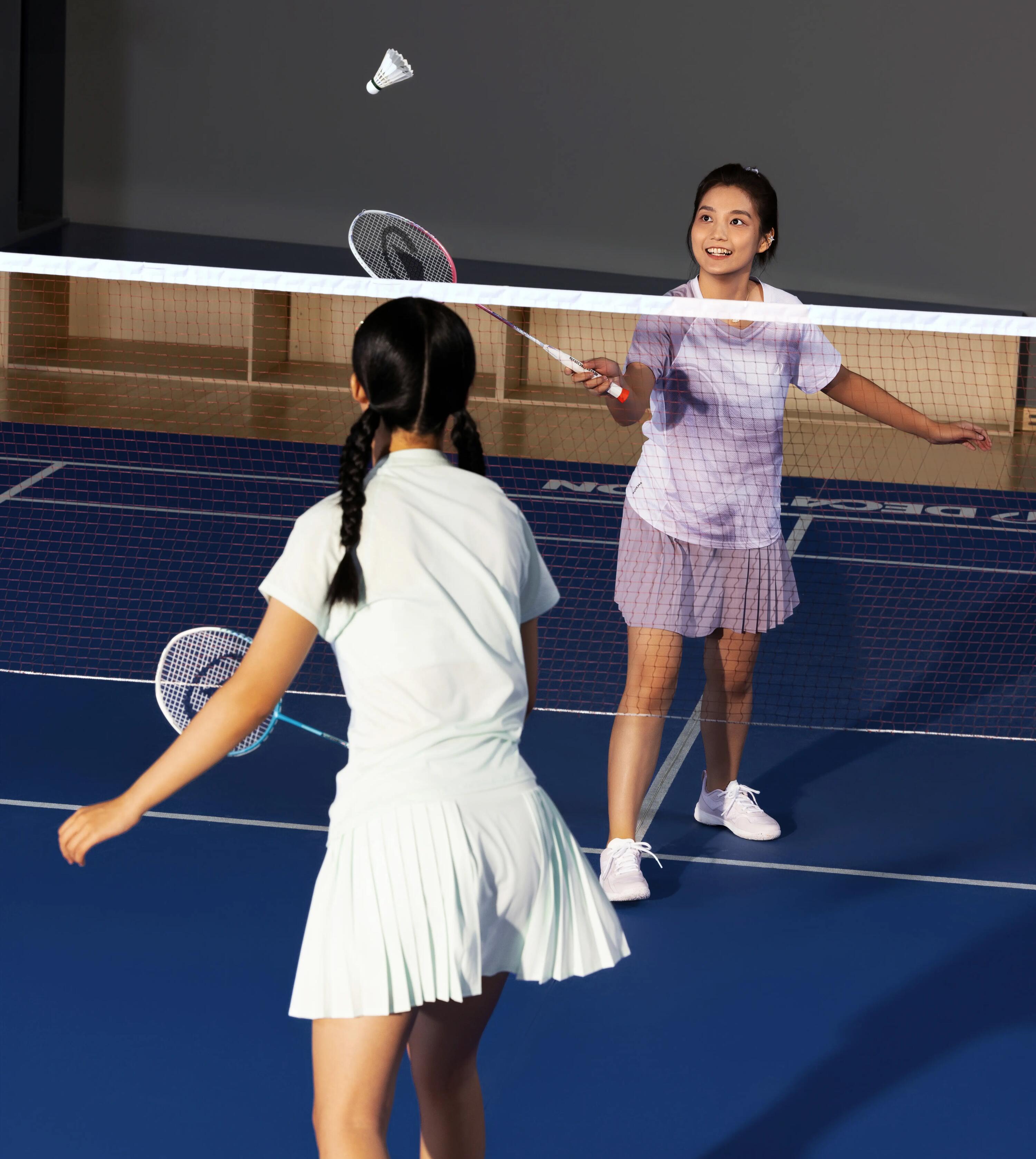 Zwei Frauen spielen Badminton in einer Halle über ein Netz.