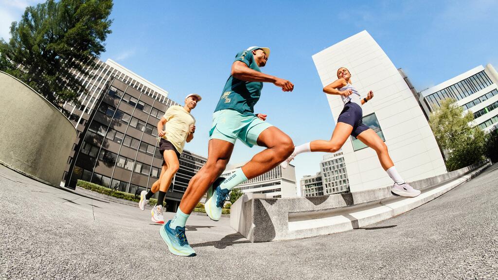 Drei Personen joggen in Sportkleidung durch eine moderne Stadt.