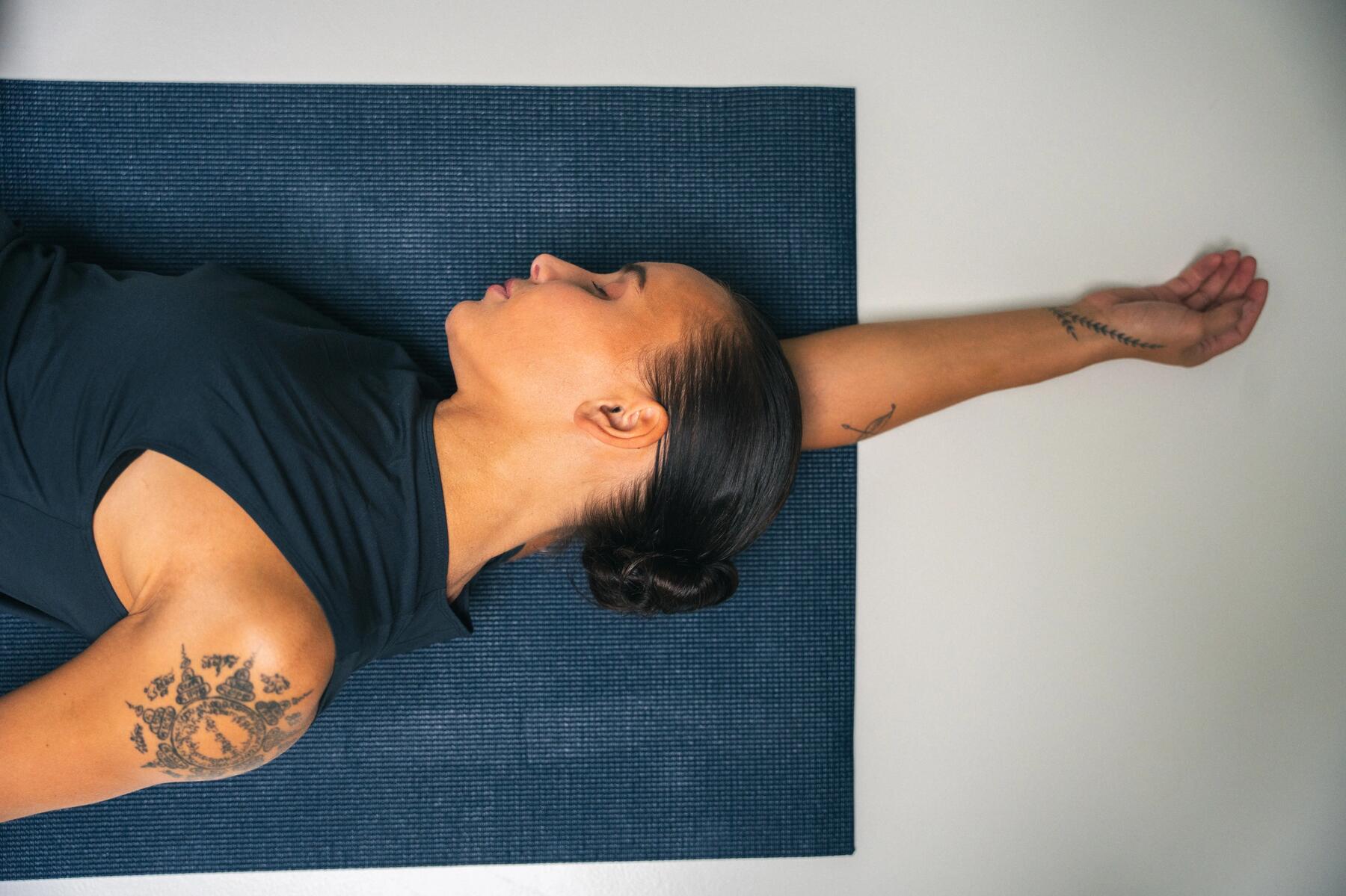 Frau auf blauer Yogamatte beim Entspannen auf dem Boden