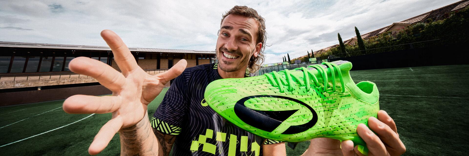 Antoine Griezmann hält ein Paar grüne KIPSTA Multinockenschuhe von Decathlon in den Händen