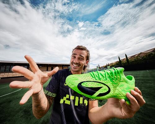 Antoine Griezmann hält ein Paar grüne KIPSTA Multinockenschuhe von Decathlon in den Händen