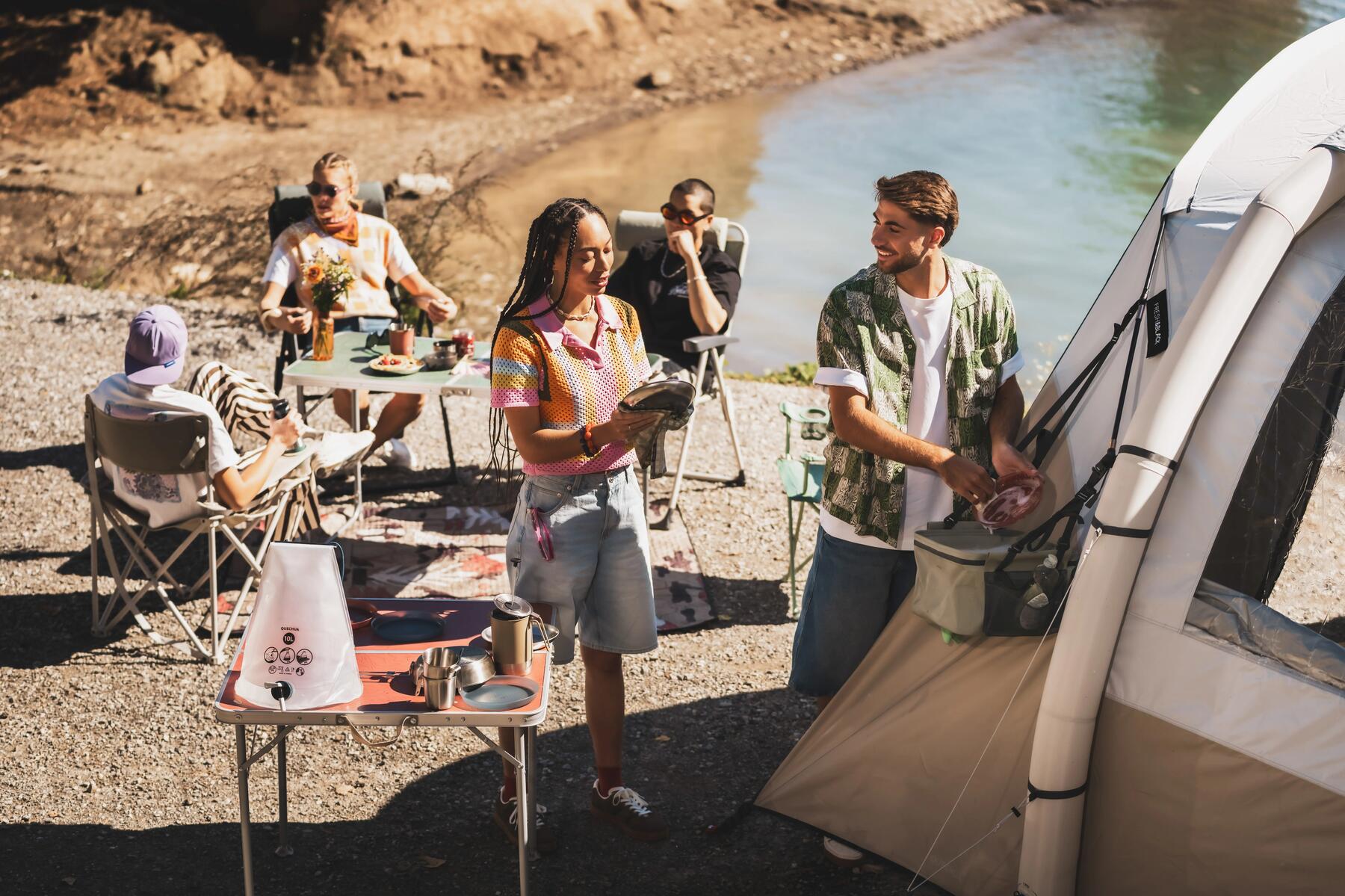Mehrere Personen sitzen vor einem Zelt und ein Mann holt etwas aus einer Camping-Kühltasche