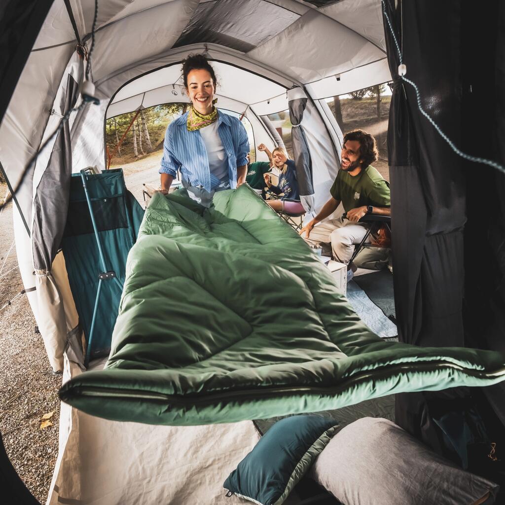 Nasmejana žena priprema zelenu Quechua Comfort vreću za spavanje unutar šatora.