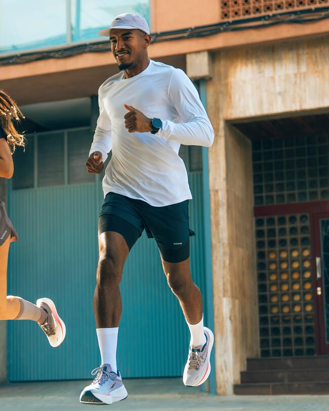 Ein Mann mit weißer Kappe und weißem Langarmshirt joggt lächelnd eine Straße entlang. 