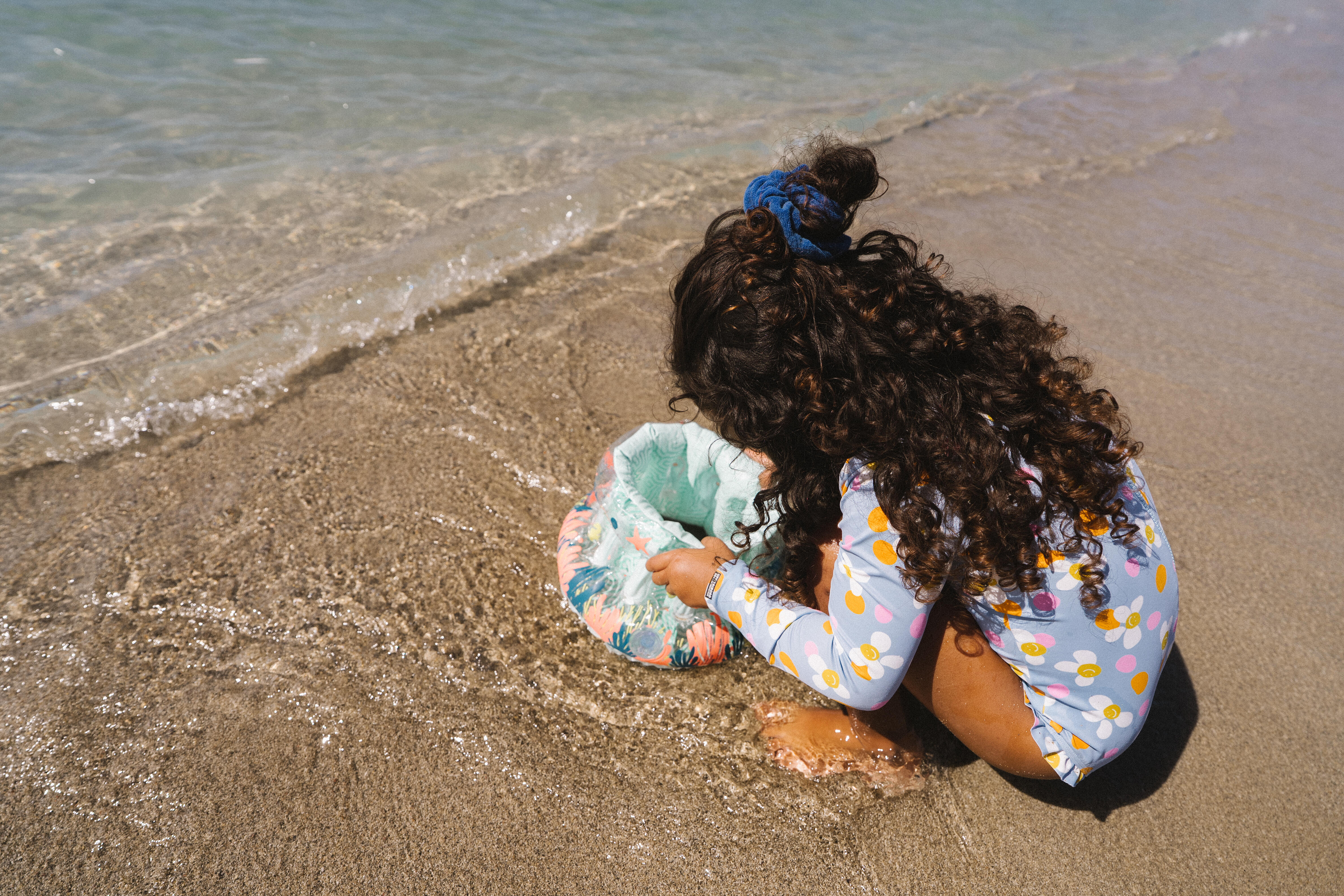 Child playing with a floating bucket in shallow water at the beach.
