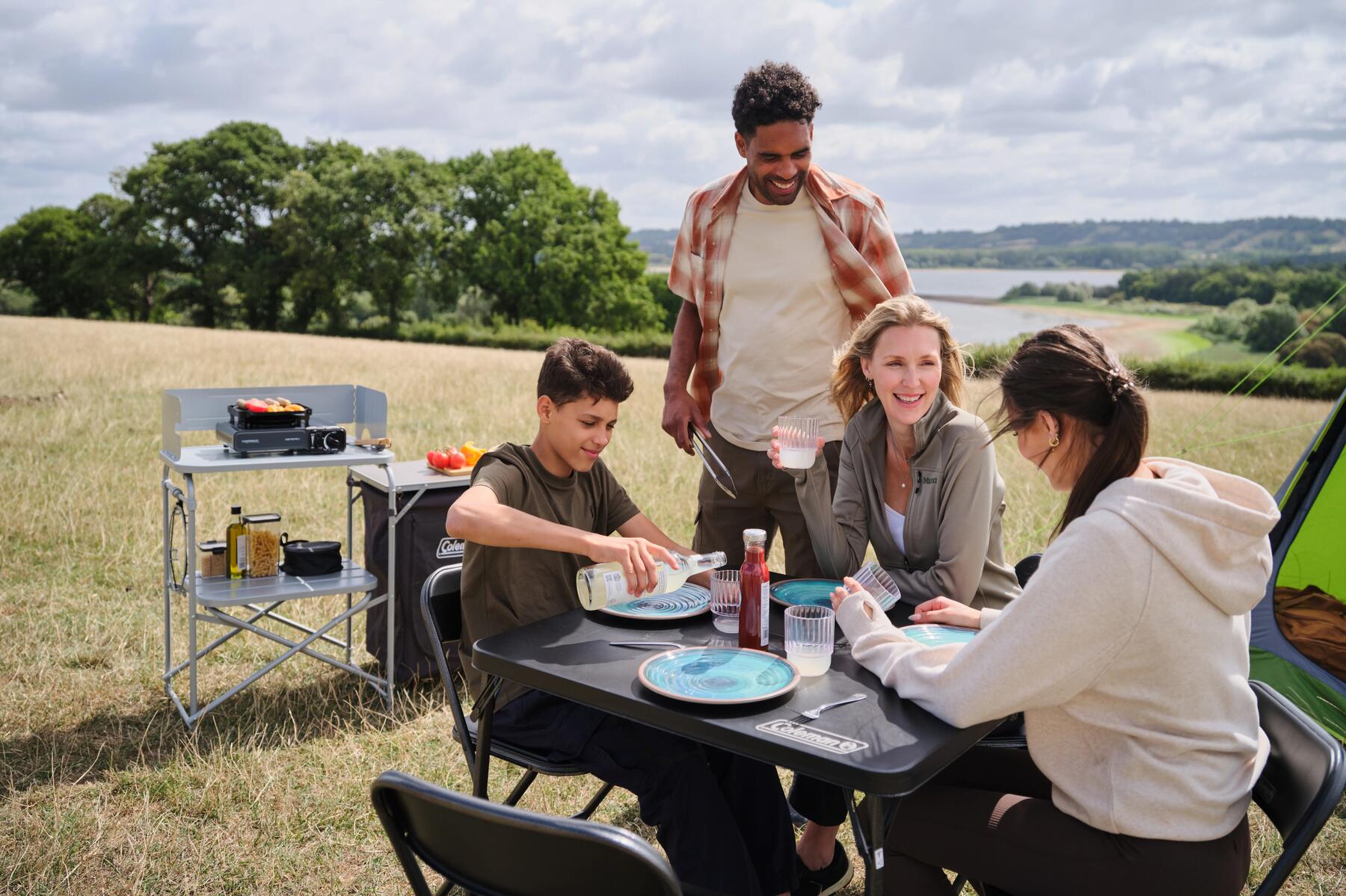Eine Familie sitzt ein einem Campingtisch und hat eine Kühltasche dabei