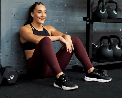 Een vrouw zit in de gym naast kettle bells met fitnessschoenen aan