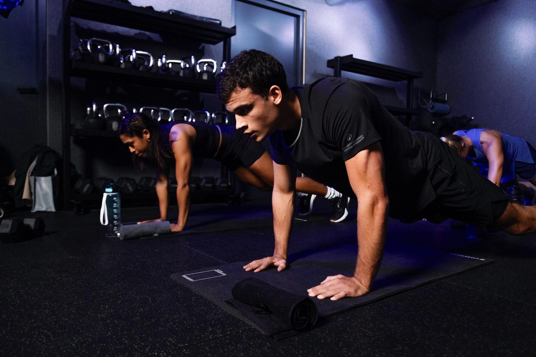 Mehrere Personen beim HIIT-Workout in einem dunklem Fitnessstudio.