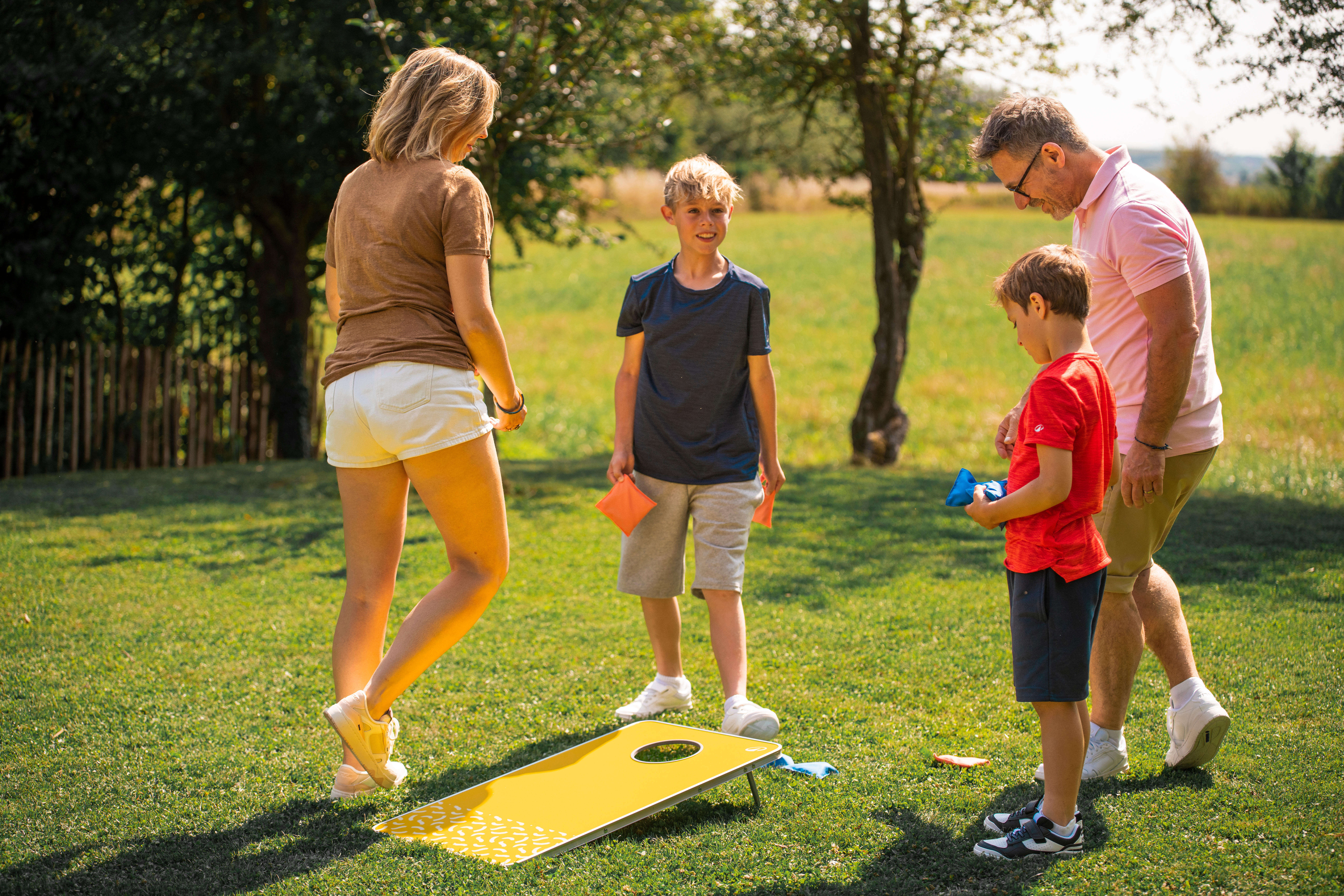 Family with two boys throwing bean bags at cornhole board