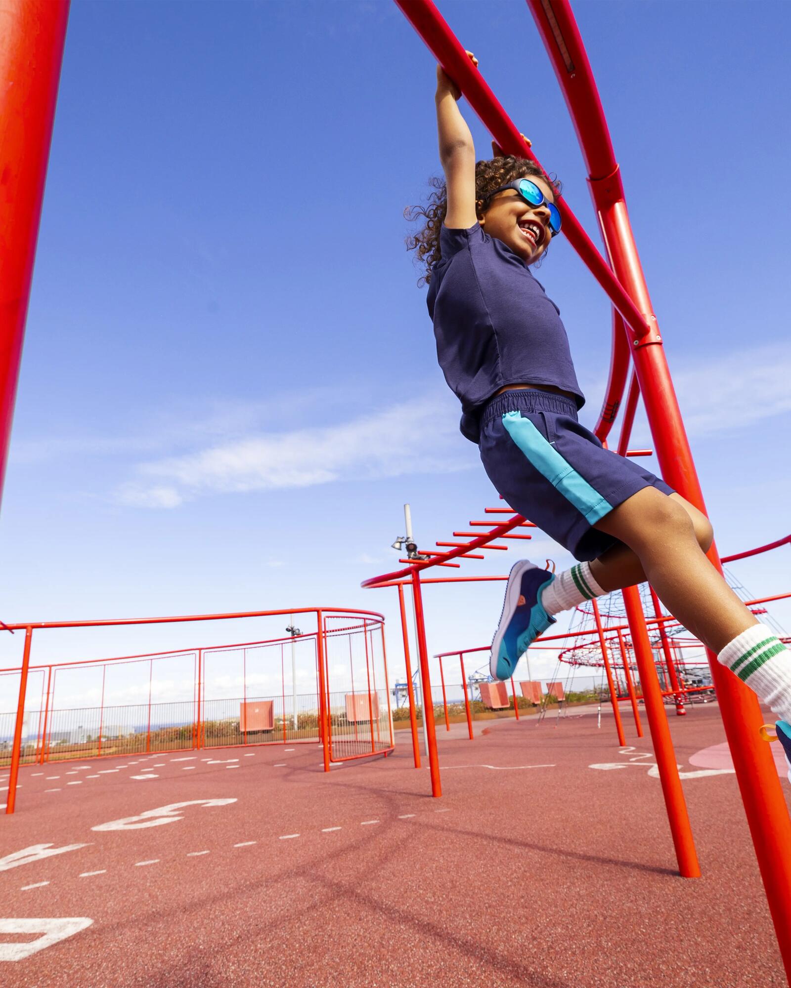 Kind auf rotem Klettergerüst mit blauen Sportschuhen auf einem Spielplatz.