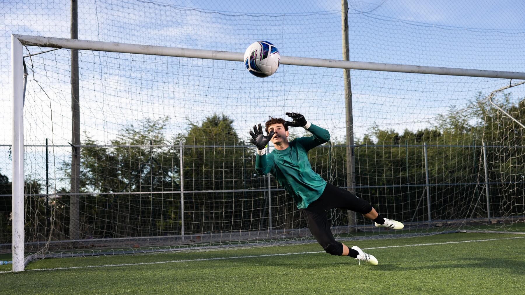 Ein Mann trägt Torwarthandschuhe und hält einen Fußball