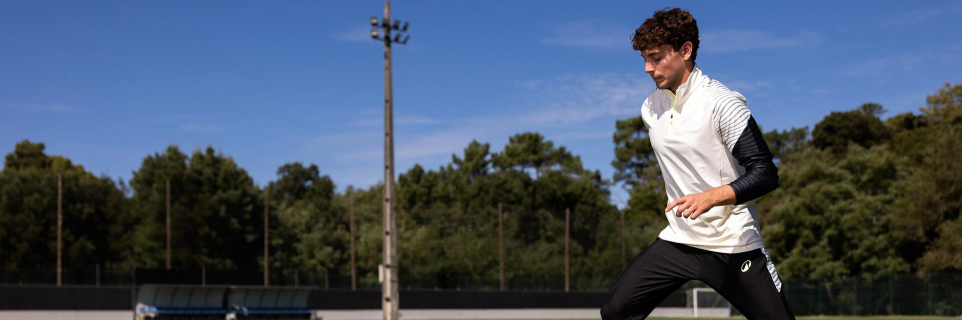 Ein Fußballspieler absolviert auf einem Sportplatz ein Trainingsprogramm mit Slalom-Hütchen und trägt dabei Fußballkleidung
