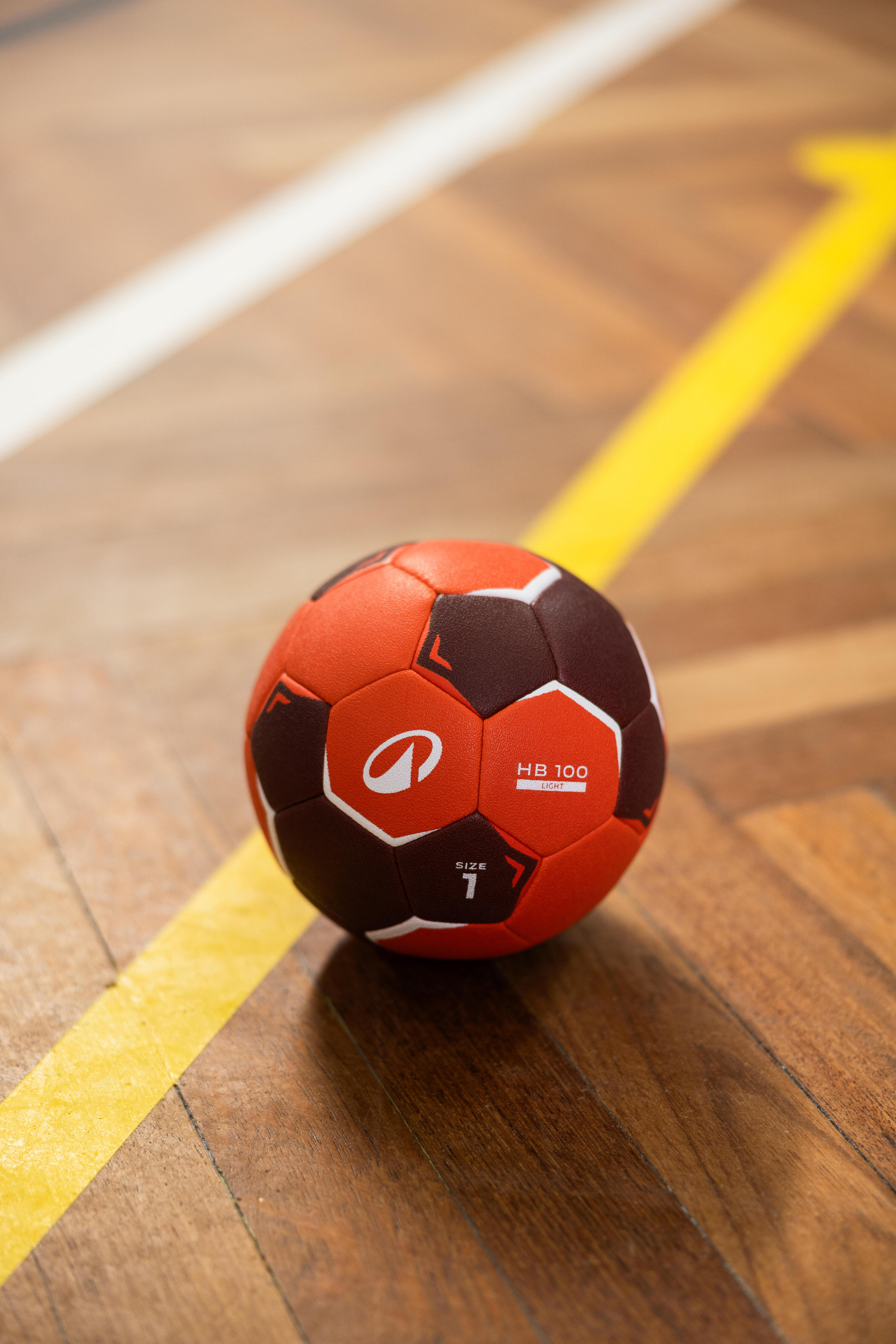 Orangener Kipsta Handball HB100 in Größe 1 auf einem Hallenboden.