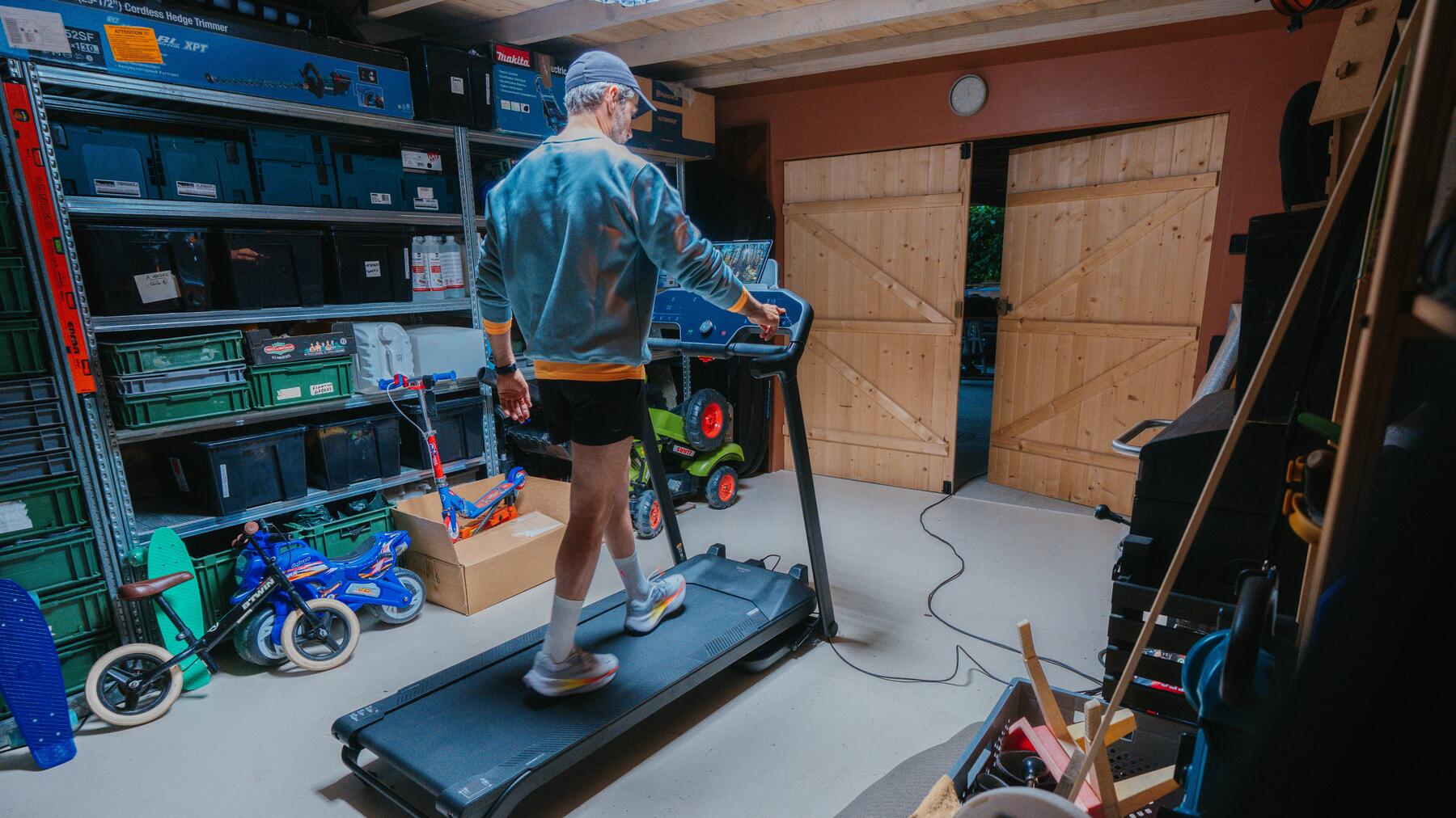 Mann in Garage auf schwarzem Laufband in kurzer Hose und weißen Laufschuhen.