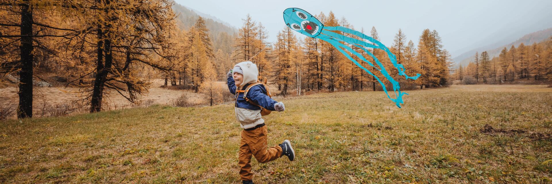 Lachendes Kind beim Drachensteigen auf einer Waldlichtung im Herbst