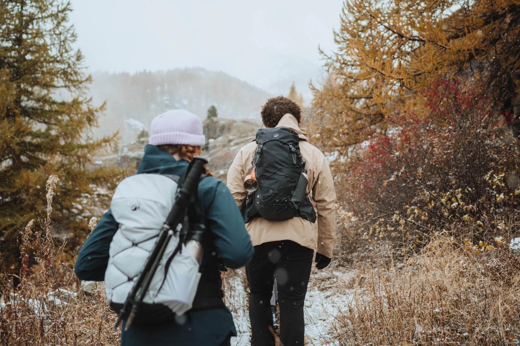 Een man en een vrouw wandelen door een natuurlandschap in de sneeuw met een rugzak en wandelstokken