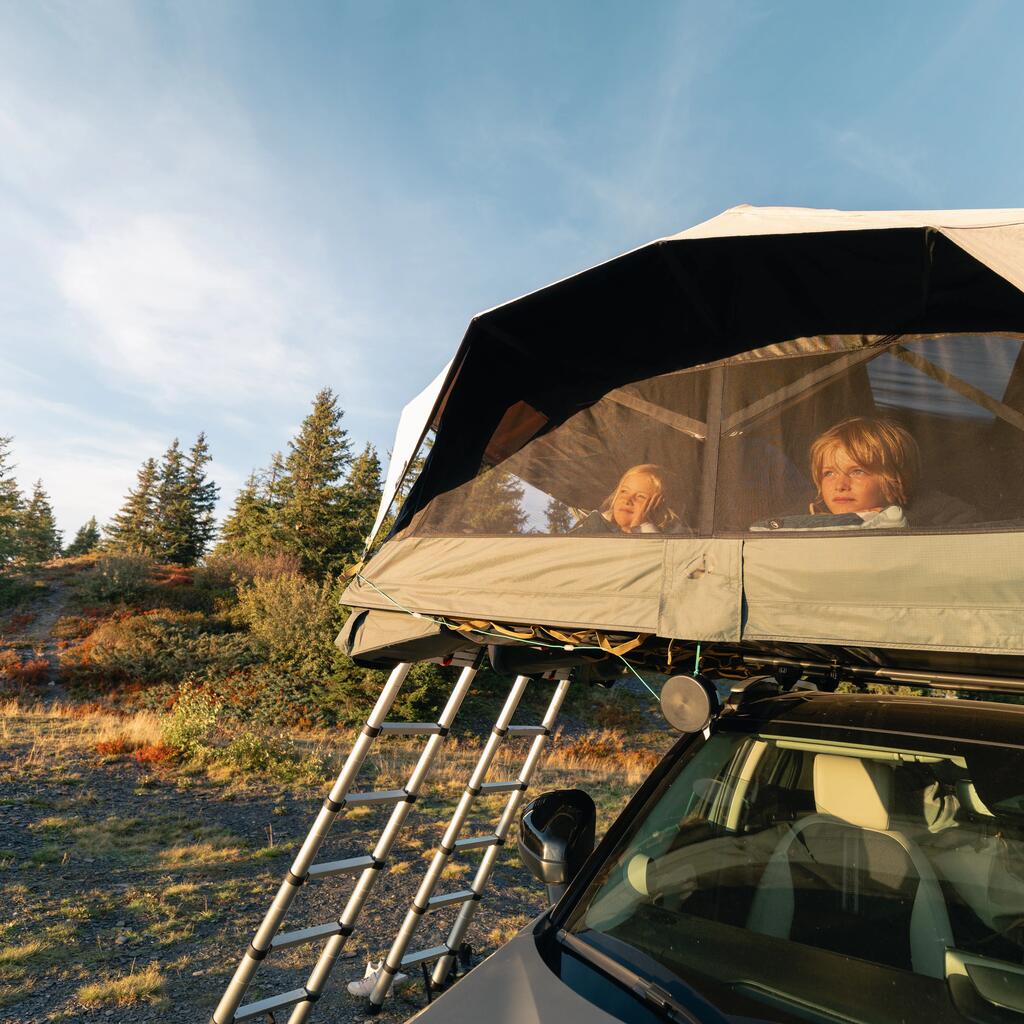 Dvoje dece gleda kroz mrežasti prozor Quechua krovnog šatora postavljenog na automobilu.