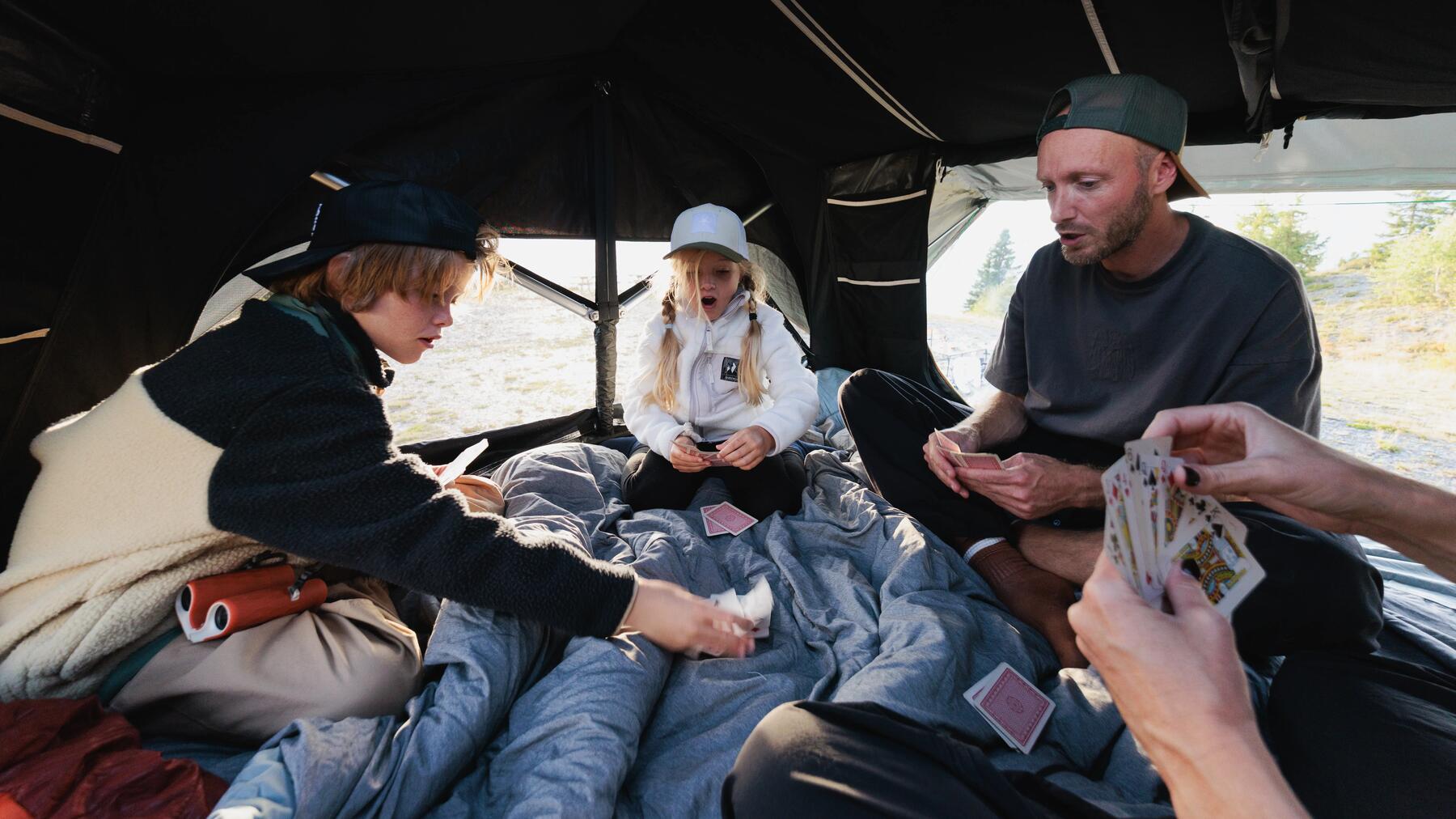 Ein Vater spielt mit seinen Kindern Karten im Zelt und nutzt Campinggeschirr