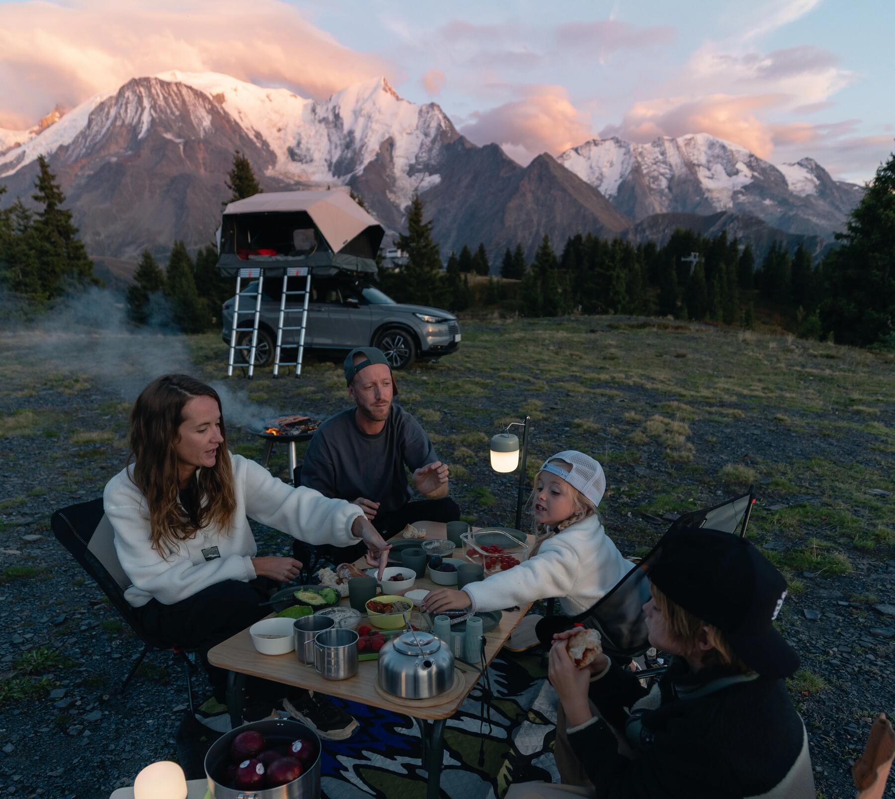 Eine Famile sitzt mit einer Campingküche in den Bergen