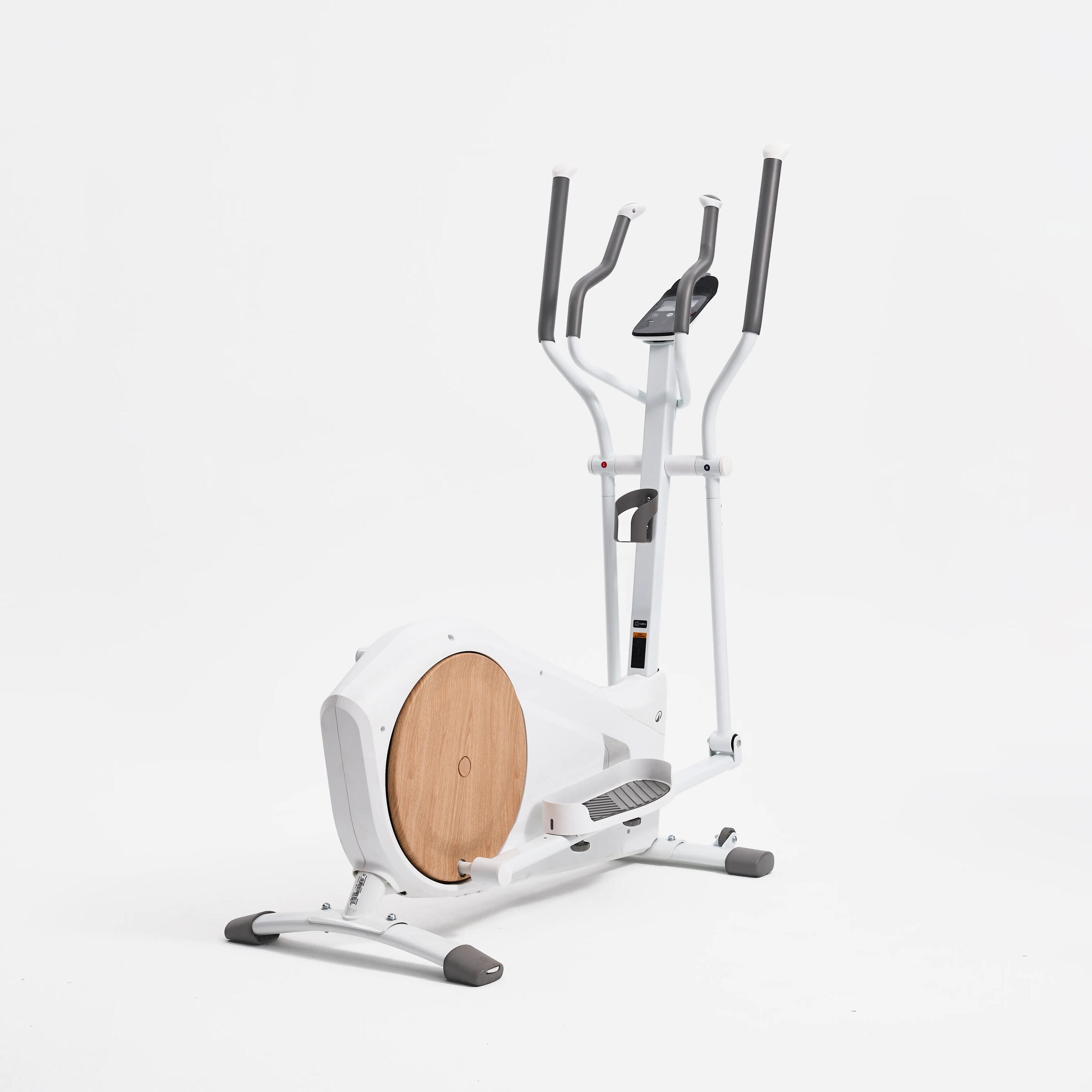 Weißer Crosstrainer mit Holzverkleidung an der Schwungscheibe vor weißem Hintergrund.