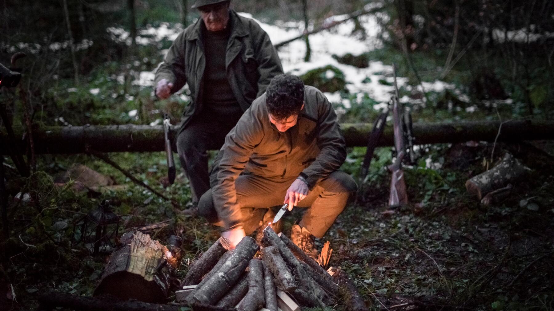 Zwei Personen nach der Jagd bei Lagerfeuer während der Dämmerung