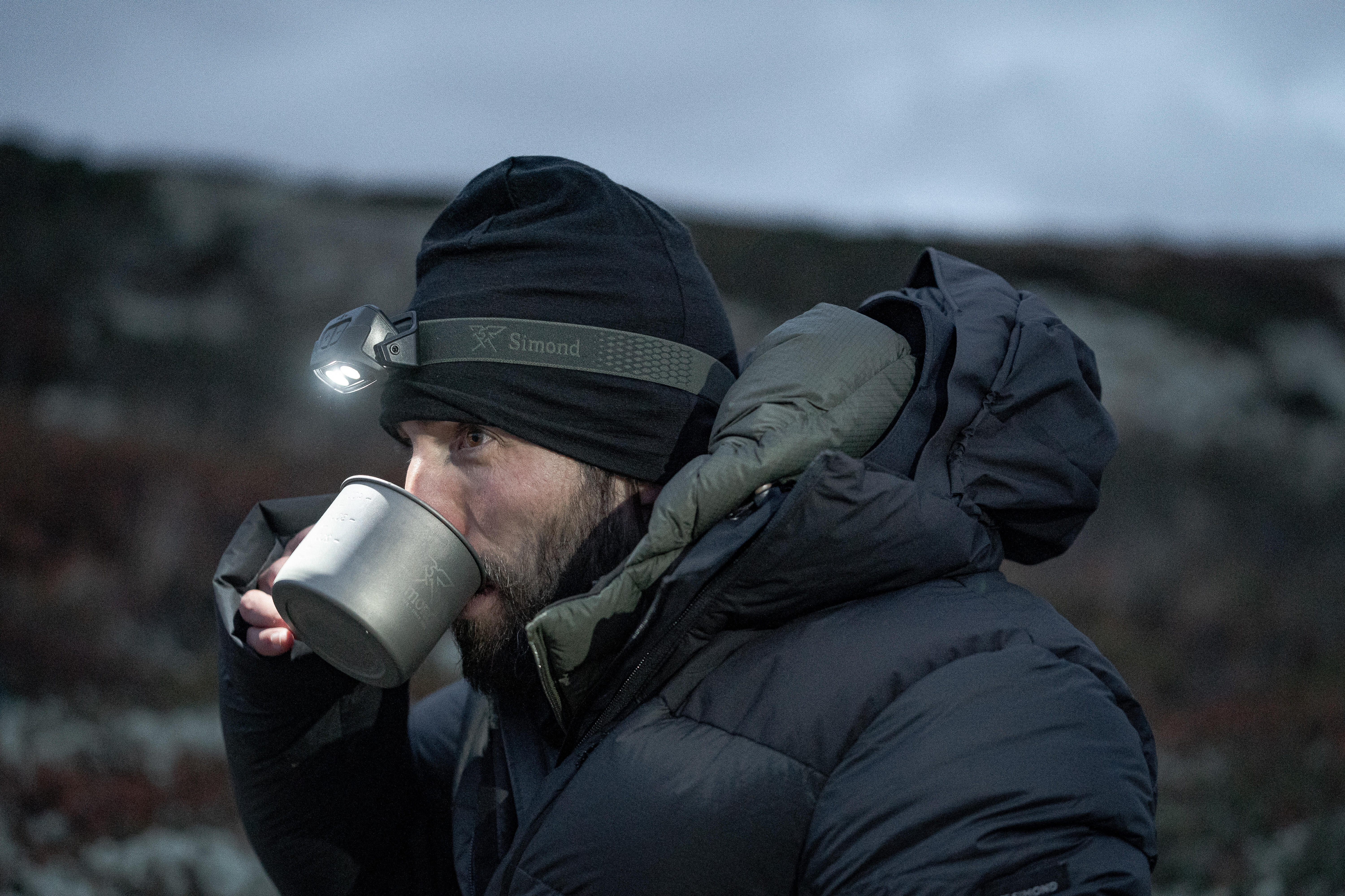 Man wearing a head torch while drinking from a mug outdoors