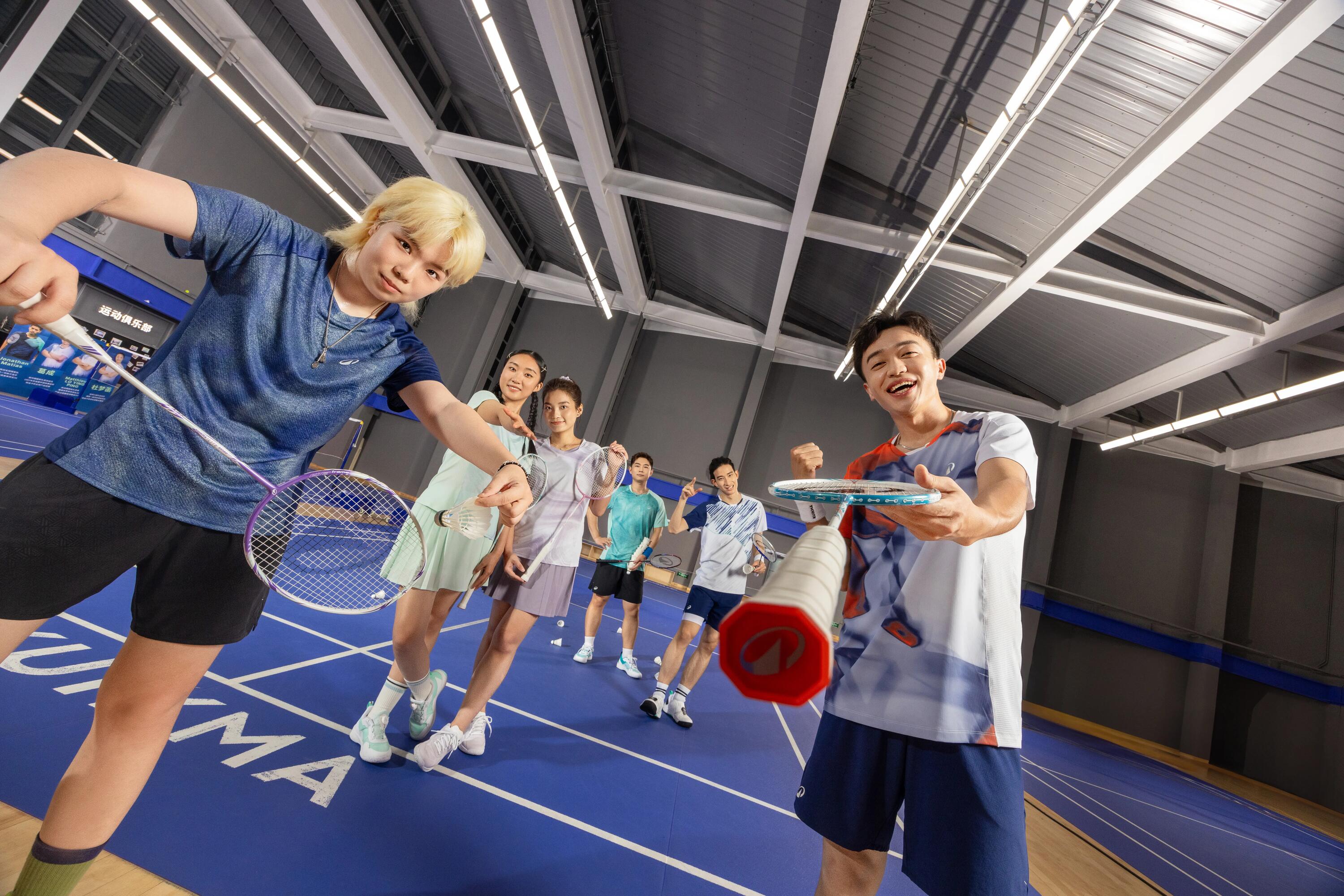 Eine Gruppe von Badmintonspielern posiert gut gelaunt mit ihren Schlägern in einer Sporthalle