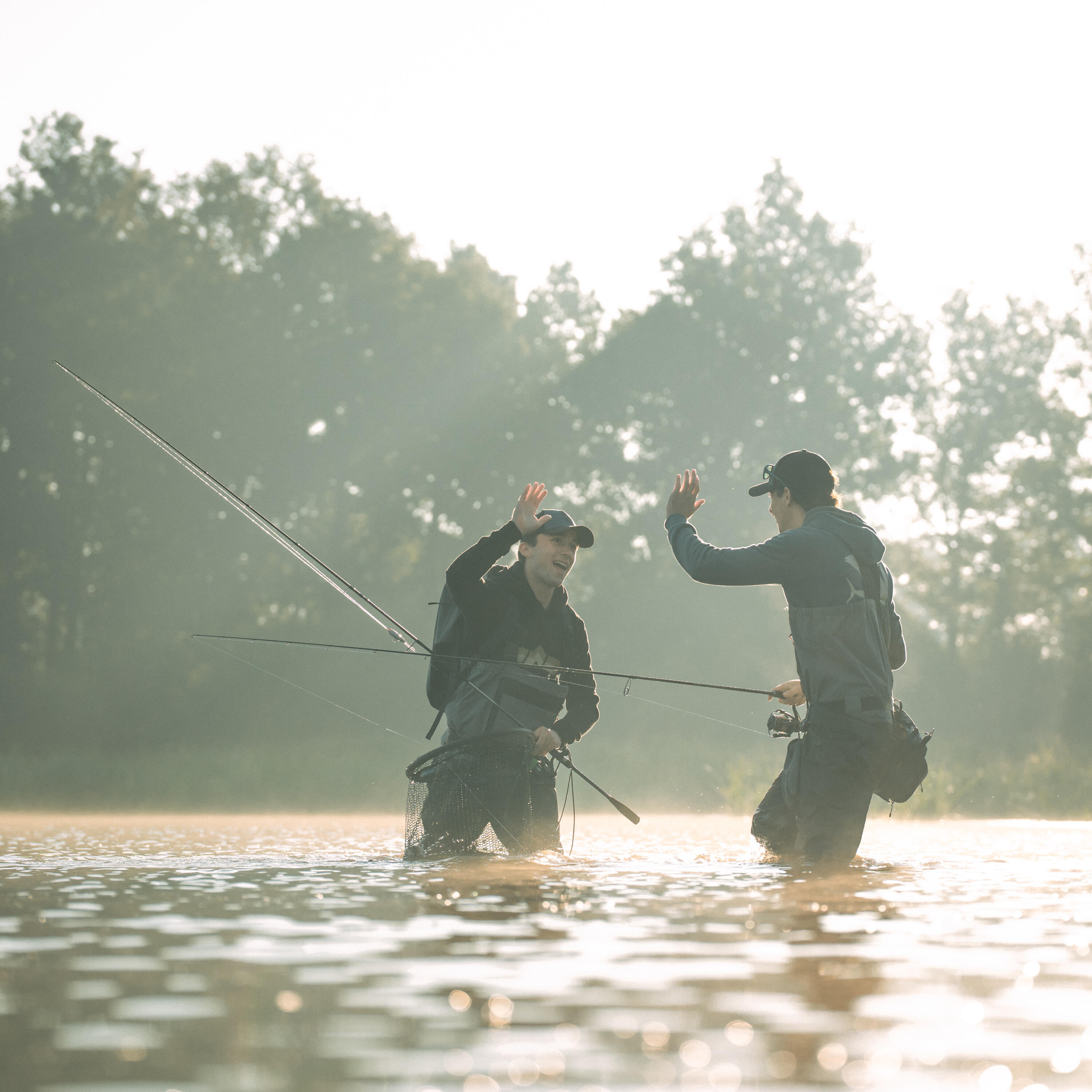 Zwei Angler stehen mit ihren Ruten im Wasser und geben sich einen "high five"