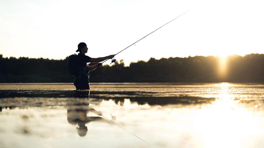 Ein Angler steht im Sonnenuntergang mit der Wathose im Wasser und angeln