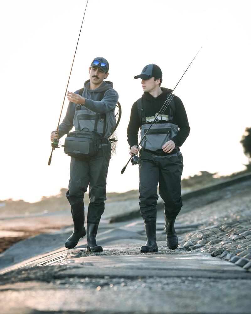 Zwei Angler laufen in Wathose am Ufer entlang