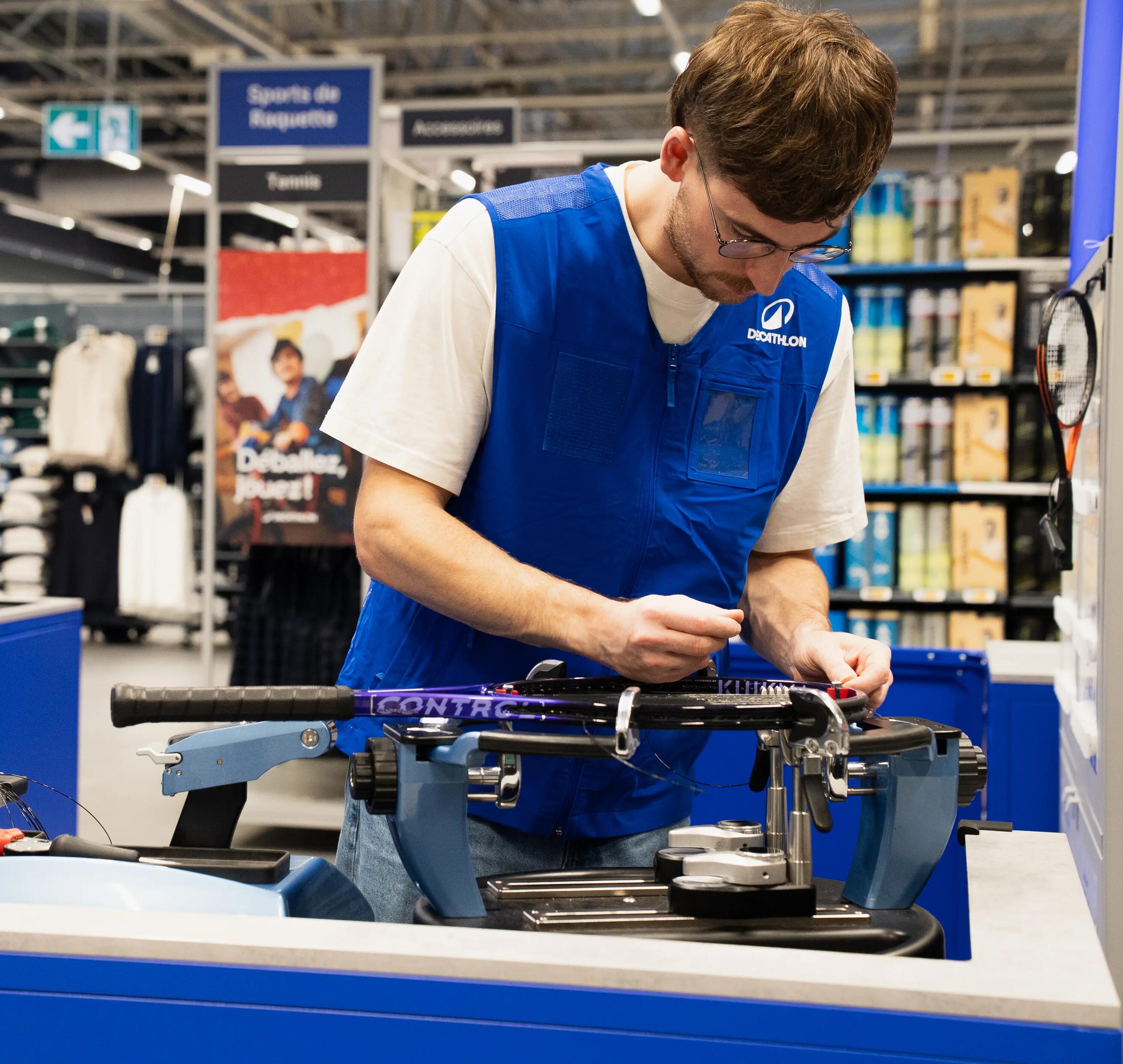 Ein Mitarbeiter im blauen Decathlon-Gilet arbeitet in einer Filiale konzentriert an einem Sportgerät.