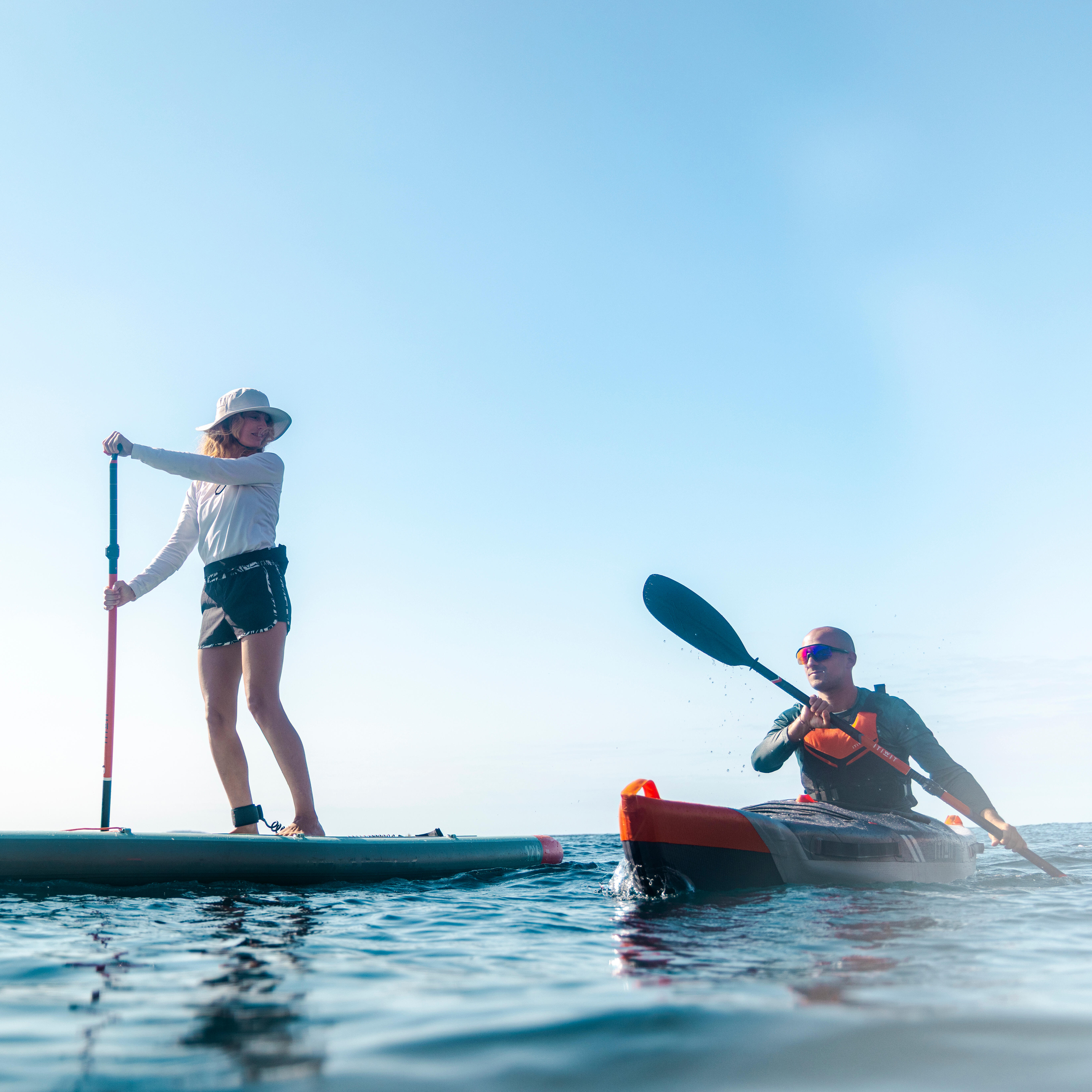 Paddle boarder and kayaker moving across calm open water
