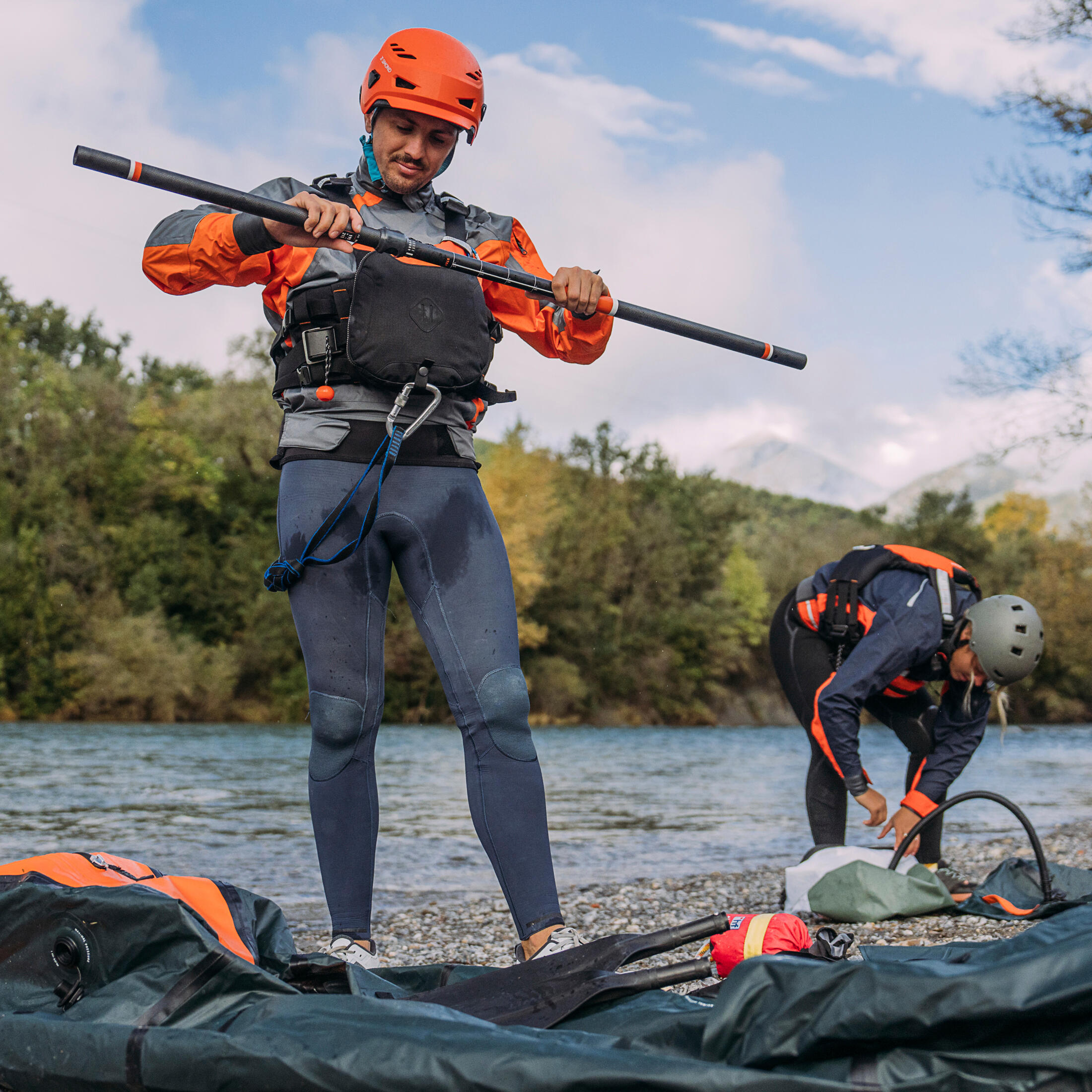 Ein Mann steht am Ufer und baut sein Kanu auf. Er hat eine Schwimmweste an und einen orangenen Helm