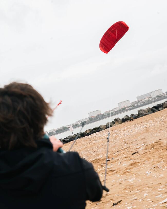 homme à la barre d'une aile de traction rouge sur la plage