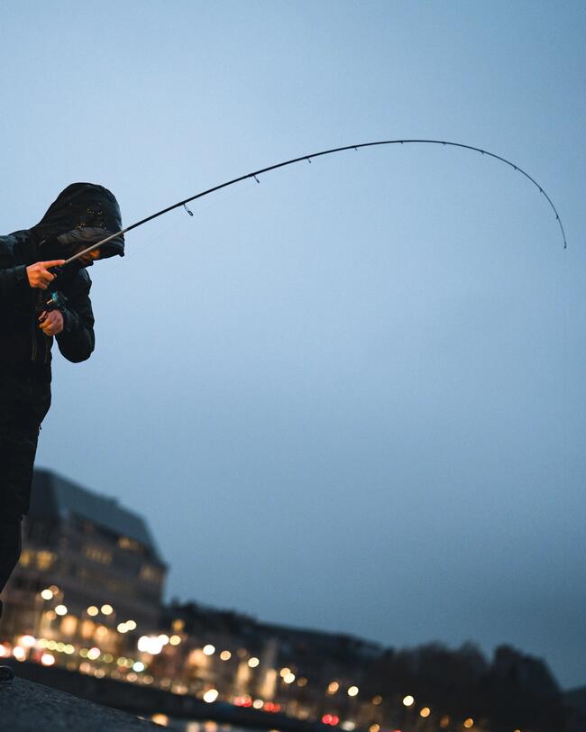 Pêcheur combattant un sandre à la nuit tombé.