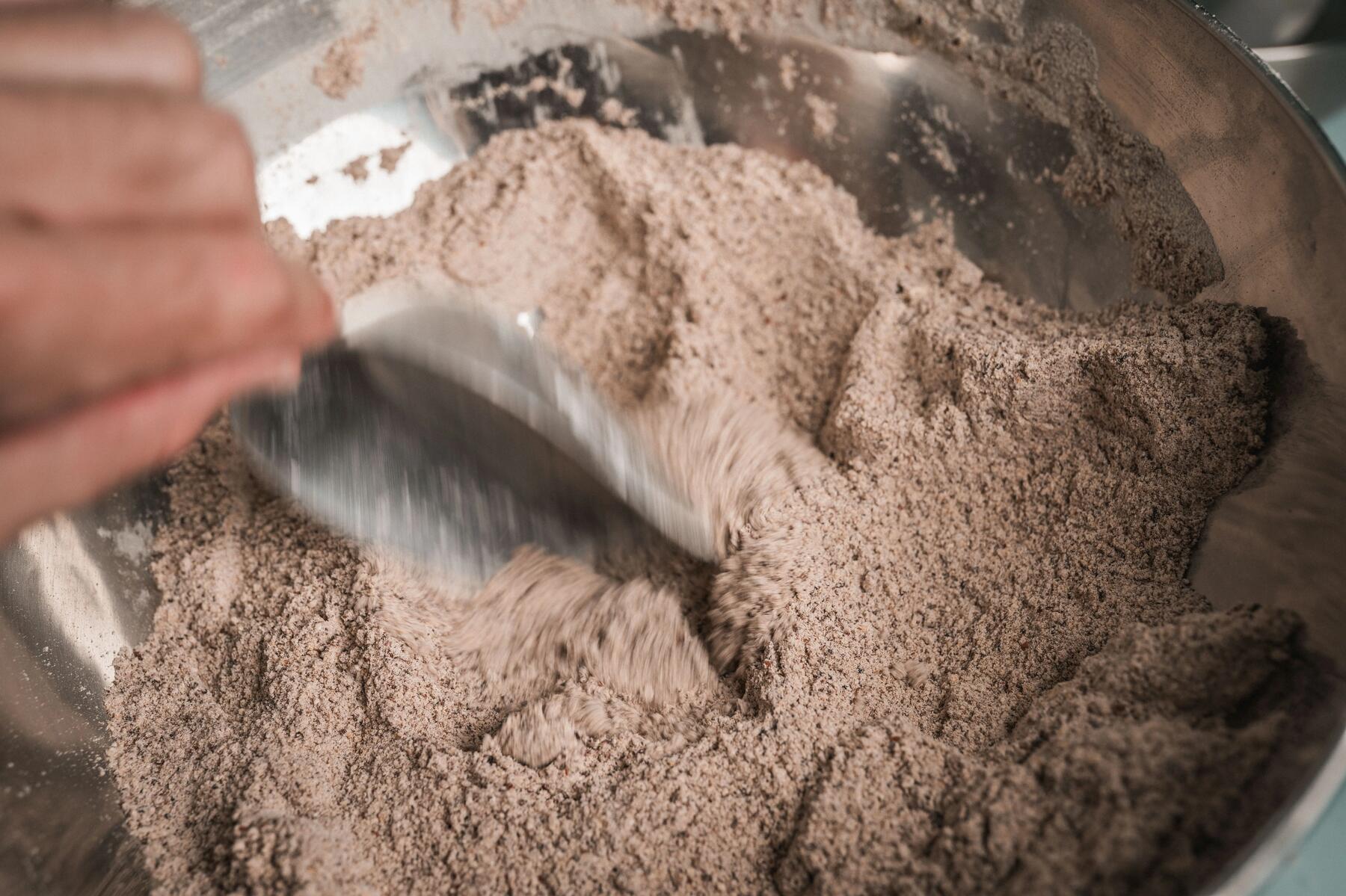 Person mischt die trockenen Zutaten in einer Edelstahl Schüssel für die Low-Carb-Cookies.