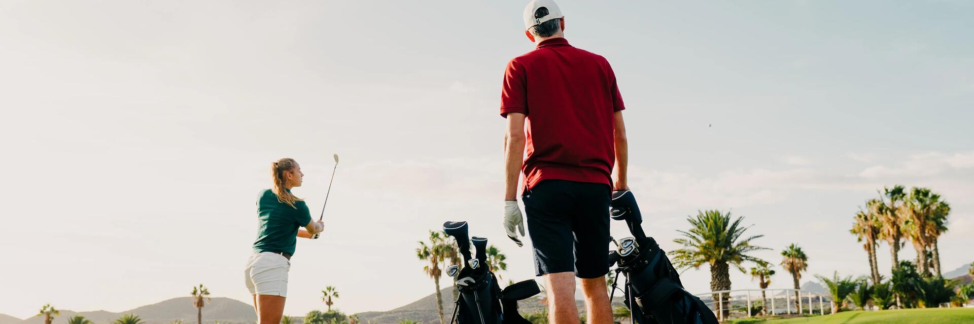 Zwei Golfer in kurzer Golfbekleidung auf dem Golfplatz mit Palmen im Hintergrund und Schläger in der Hand.