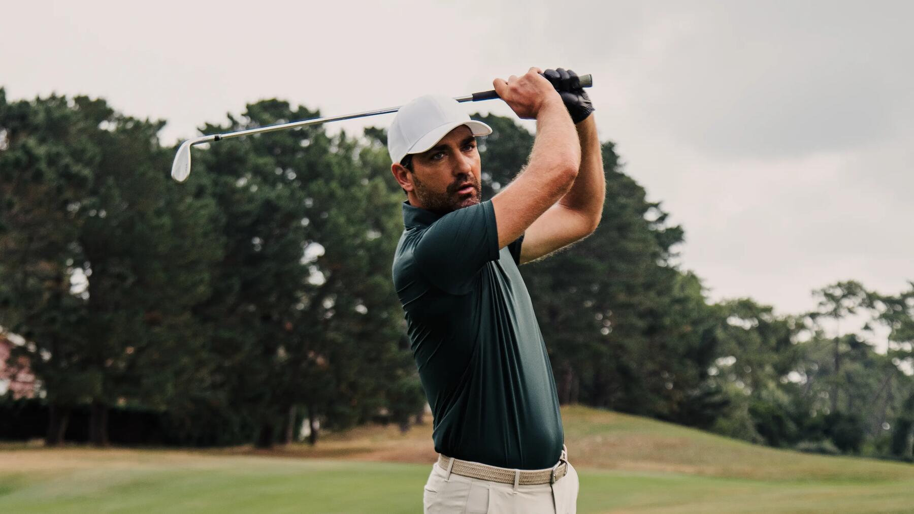 Golfer in grünem Polo mit weißer Cap beim Ausholen mit dem Golfschläger.